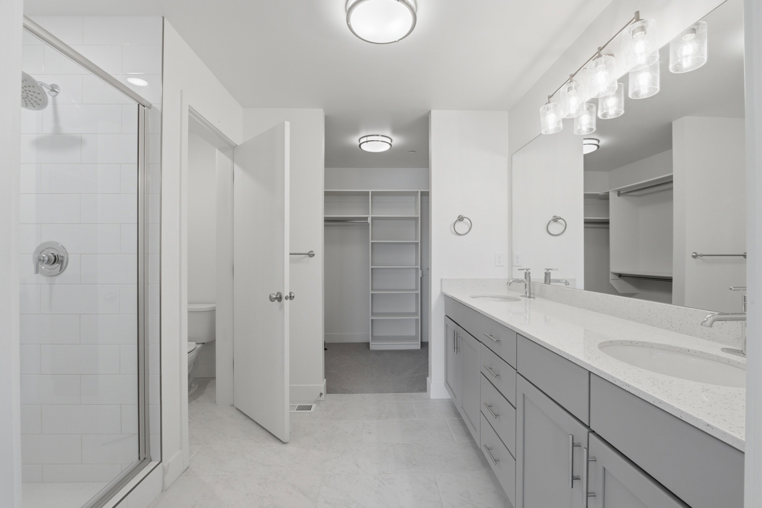 Primary ensuite bathroom with double vanity, grey cabinetry and white quartz countertops