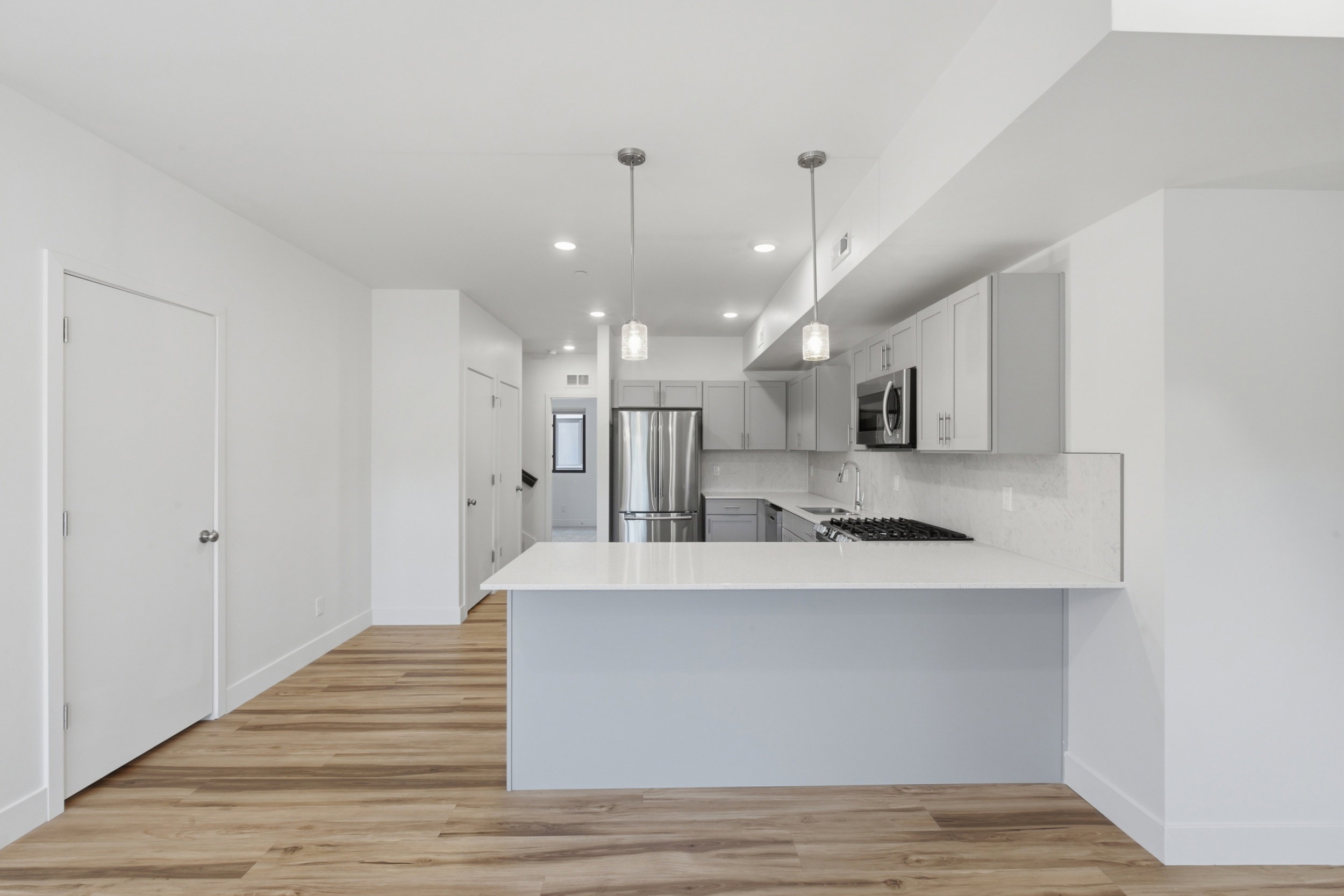 Open-concept kitchen featuring gray cabinetry, stainless steel appliances, white quartz countertops, and a tile backsplash