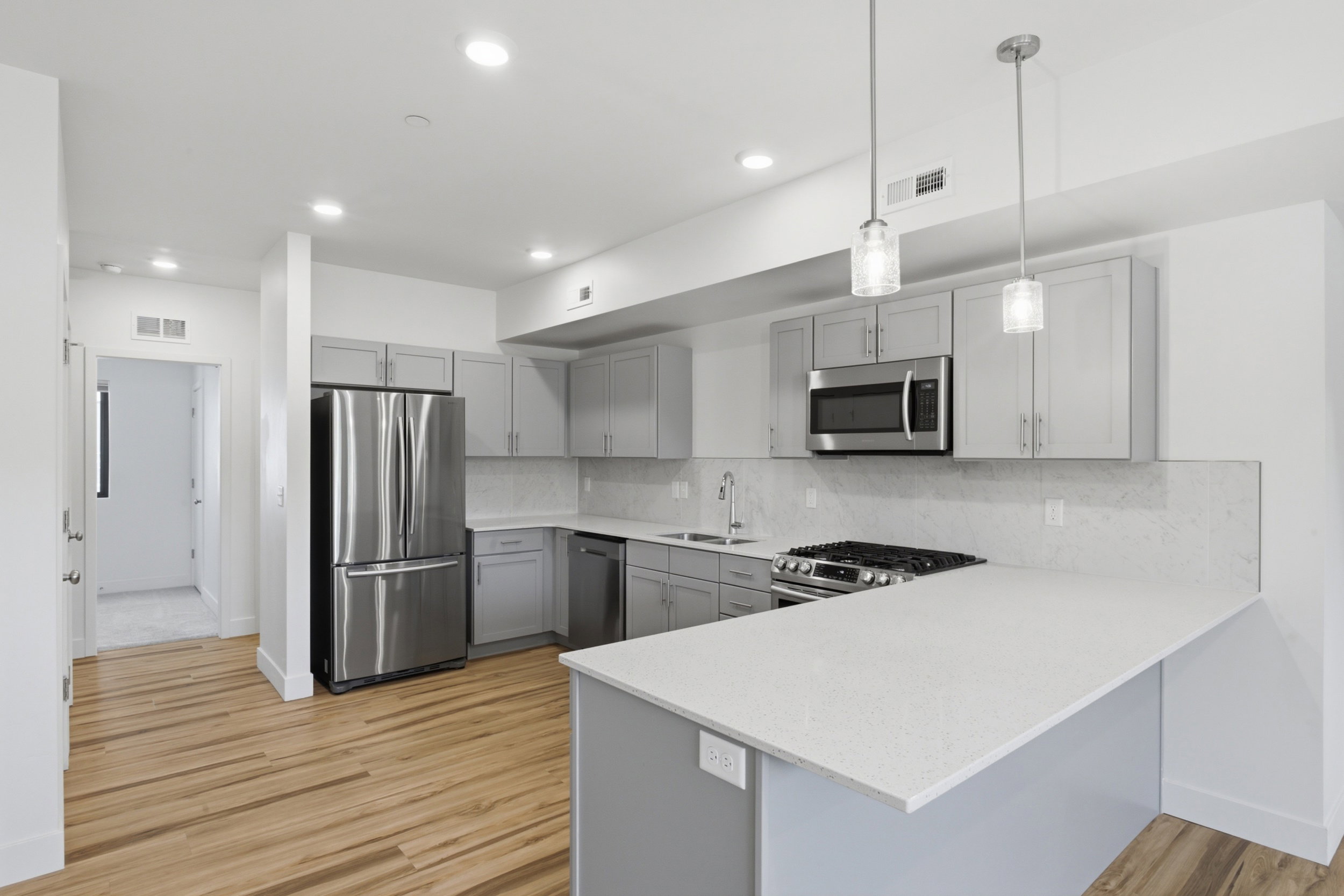 Modern kitchen featuring stainless steel appliances, light gray cabinetry, quartz countertops, and a gas range