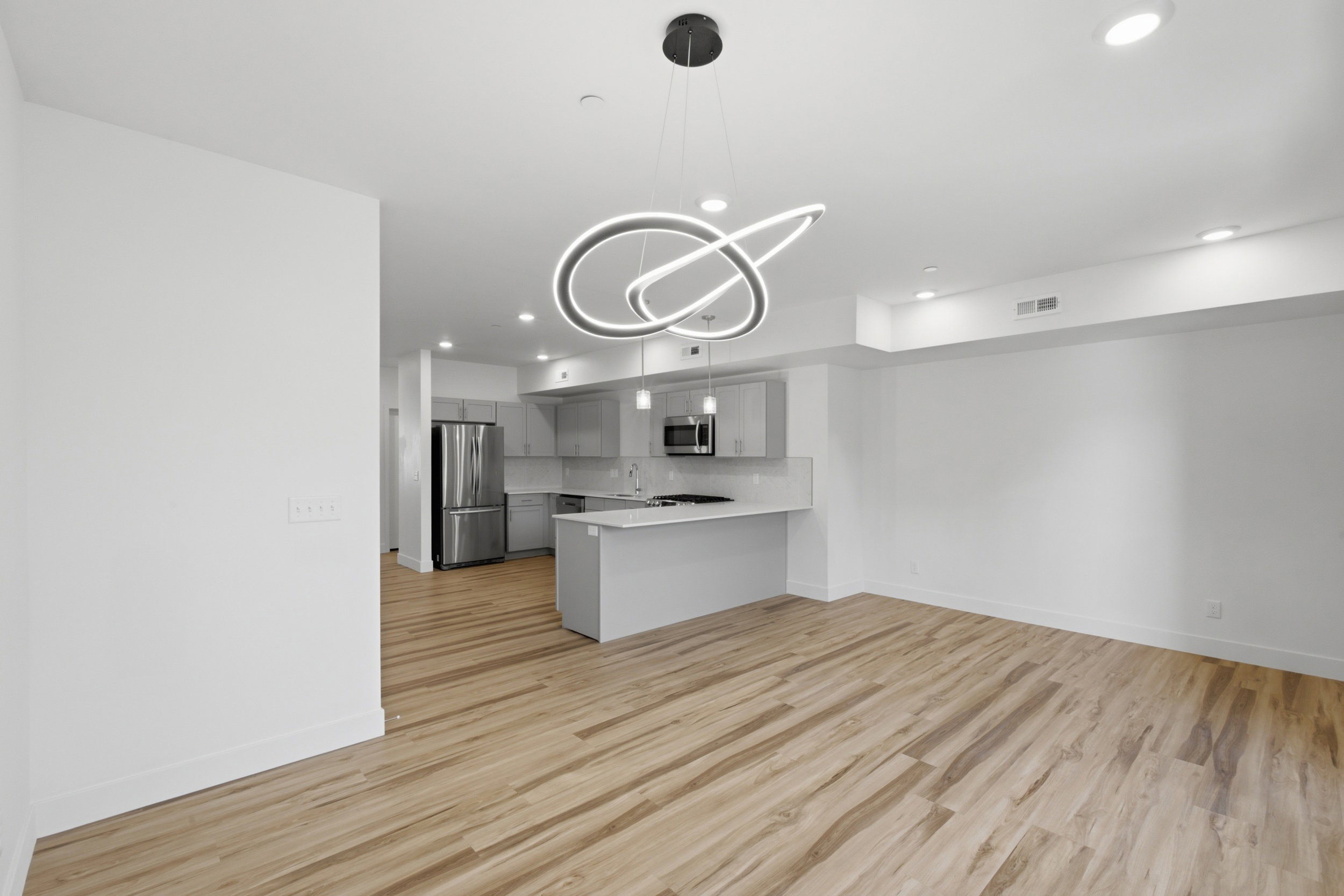 Open-concept living space featuring wood-finish flooring, a modern chandelier, recessed lighting, and a kitchen with stainless steel appliances