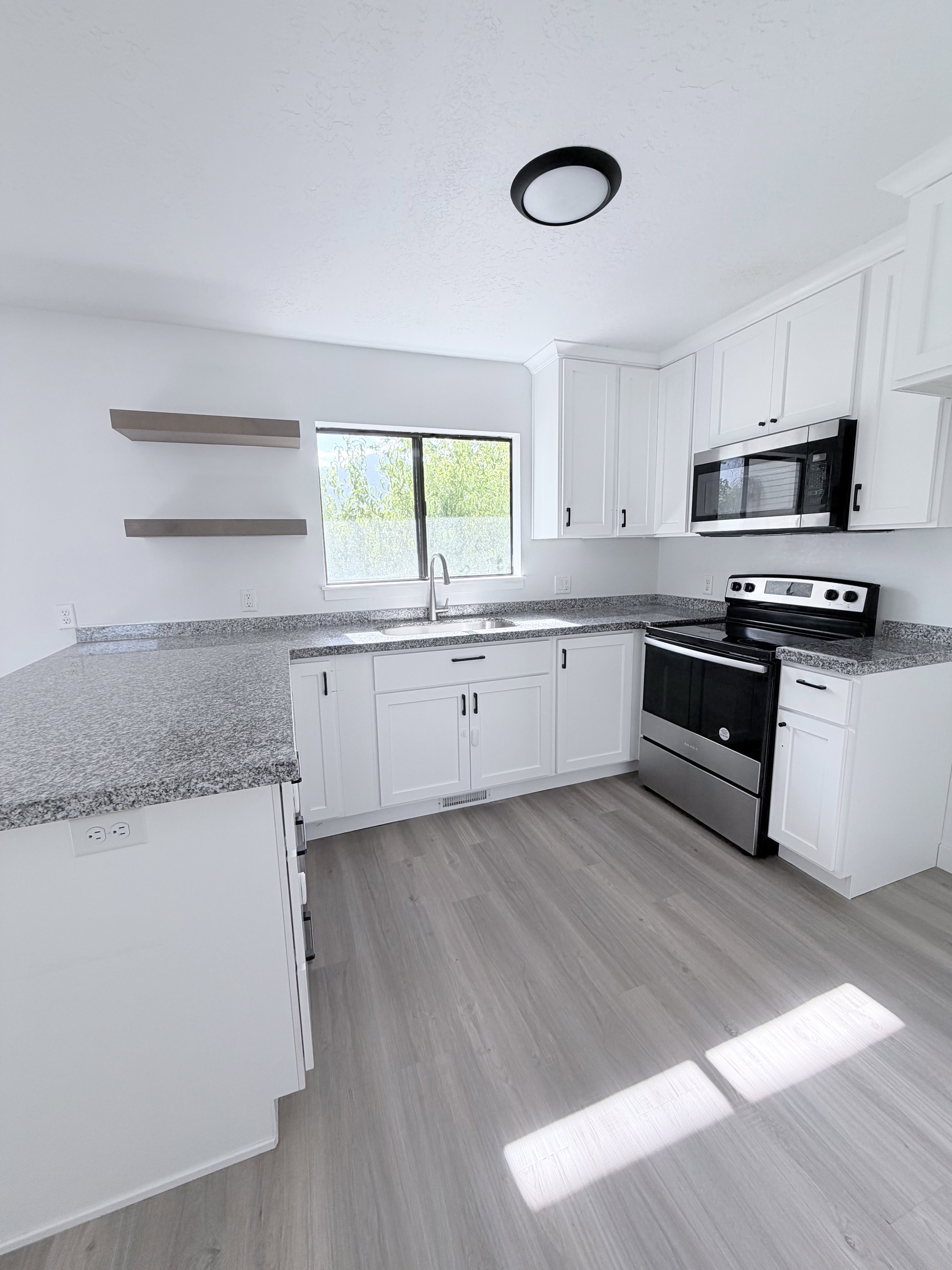 Kitchen featuring white cabinetry, grey speckled countertops, stainless steel appliances, and wood-finish flooring