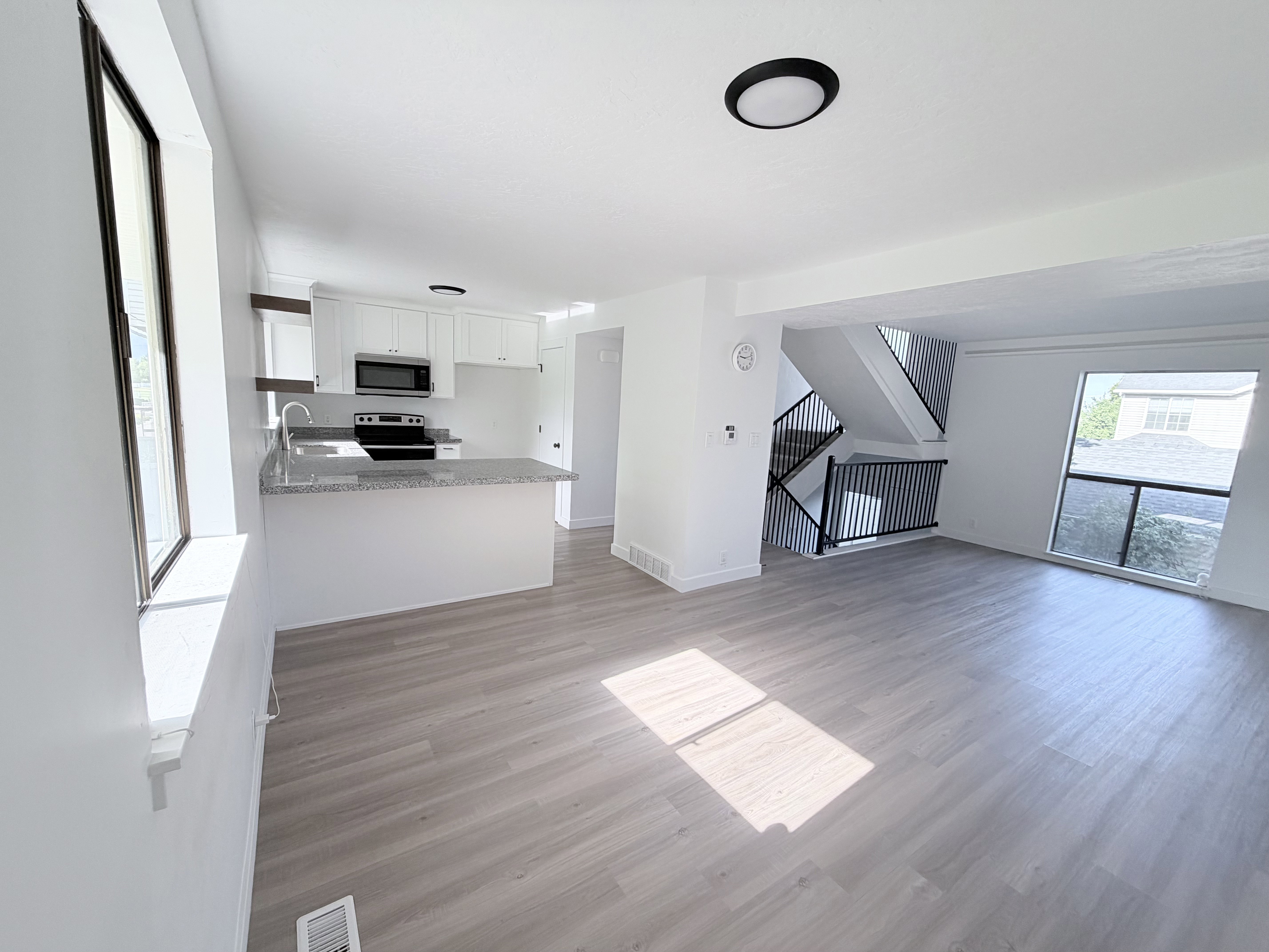Open-concept living area featuring light wood-finish flooring, white walls, and a modern kitchen with white cabinetry and a breakfast bar