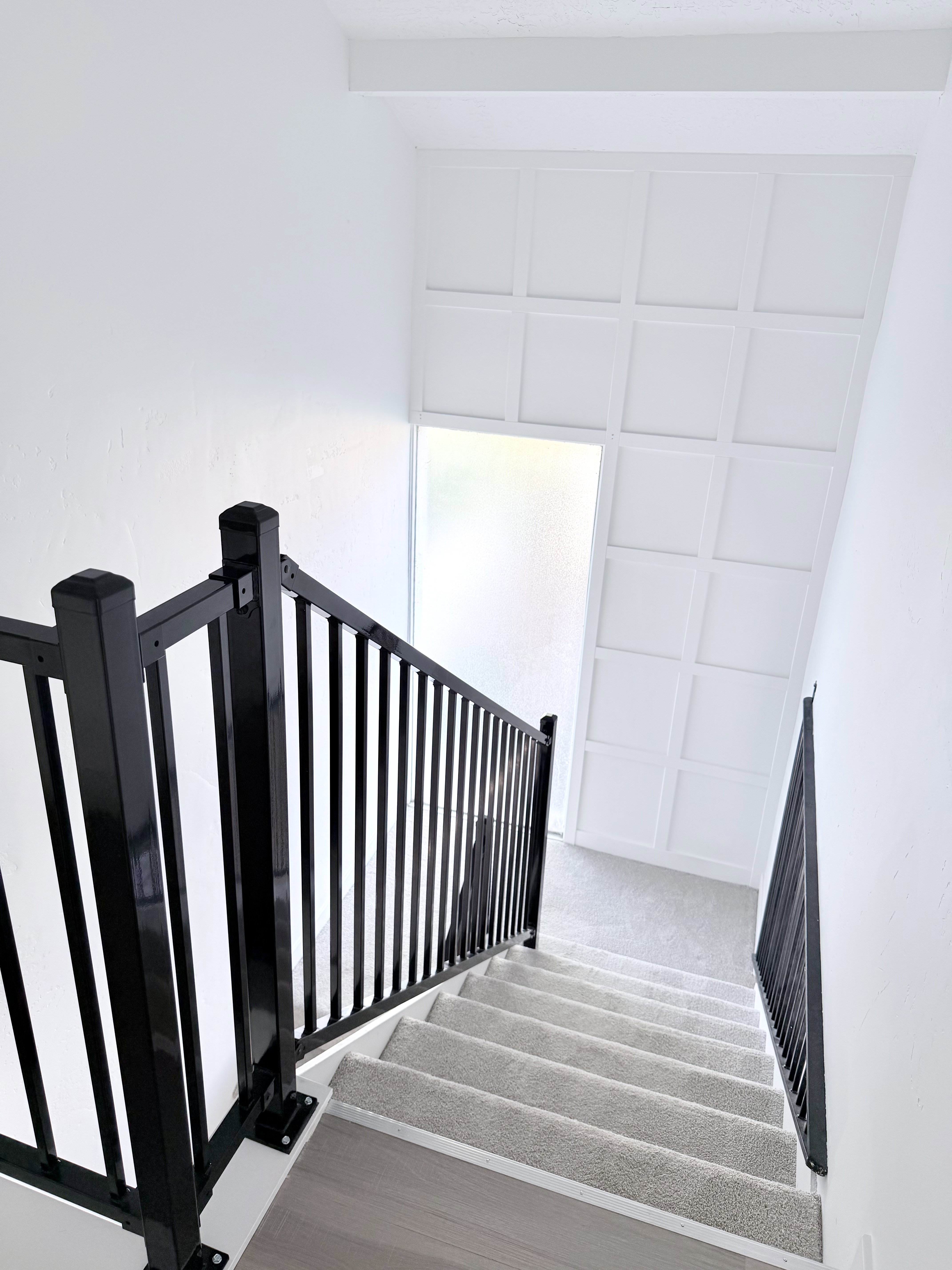 Staircase featuring dark metal railings and light-colored carpeted treads with wood-finish risers
