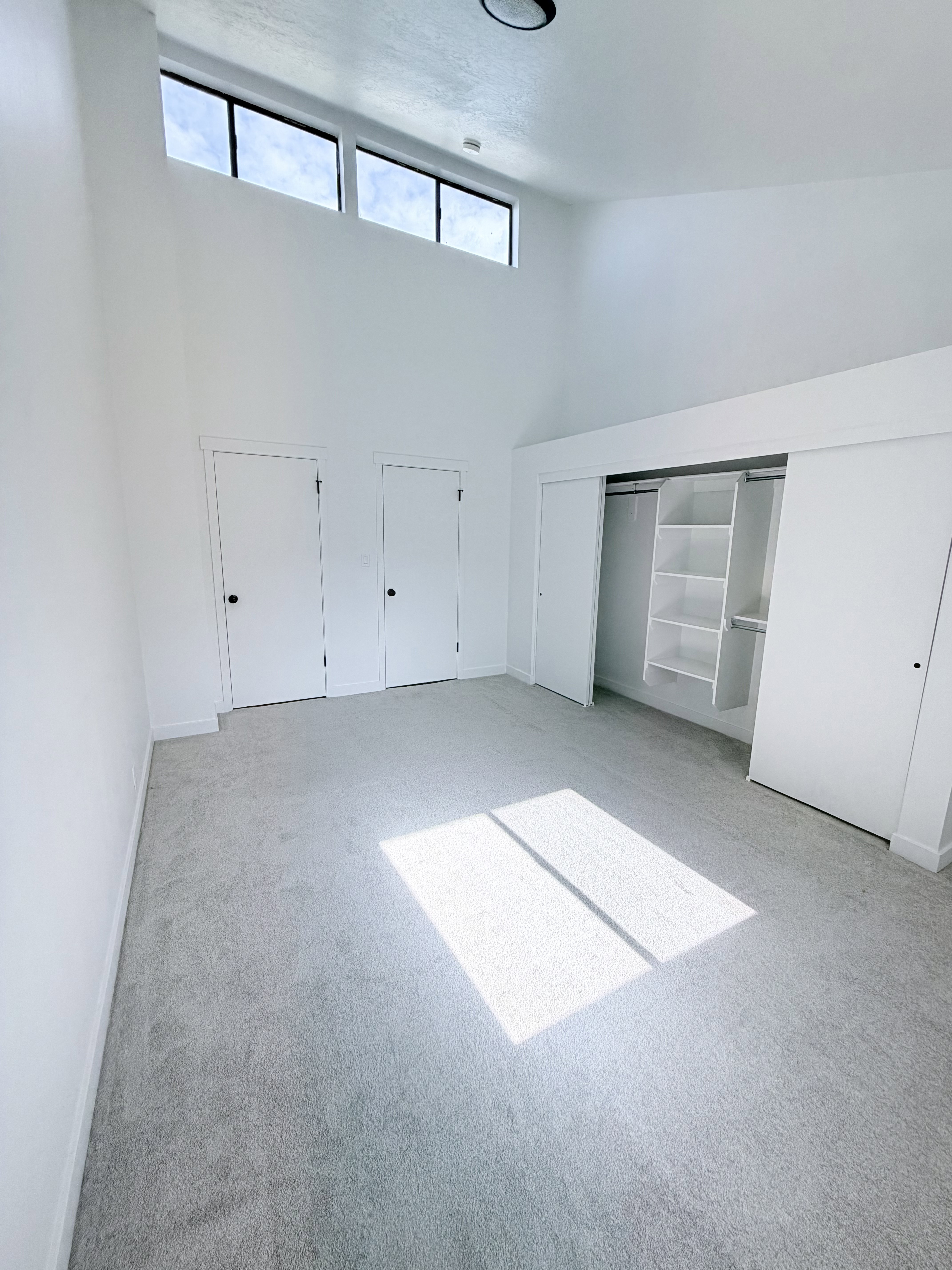 Spacious room featuring a vaulted ceiling with clerestory windows, light gray carpeting, and a built-in closet system with shelving