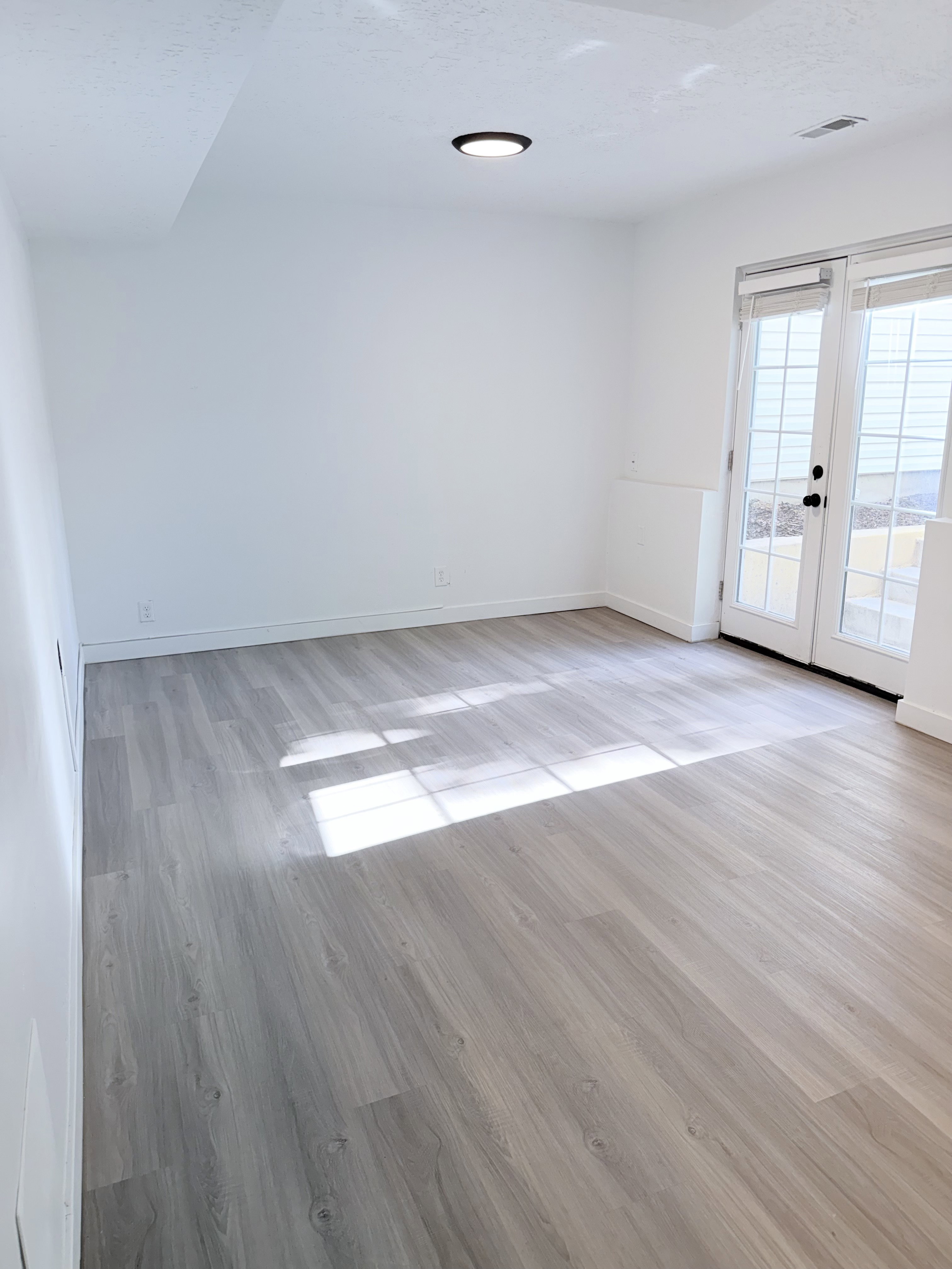 Spacious room with wood-finish flooring, white walls, and a contemporary flush-mount ceiling light