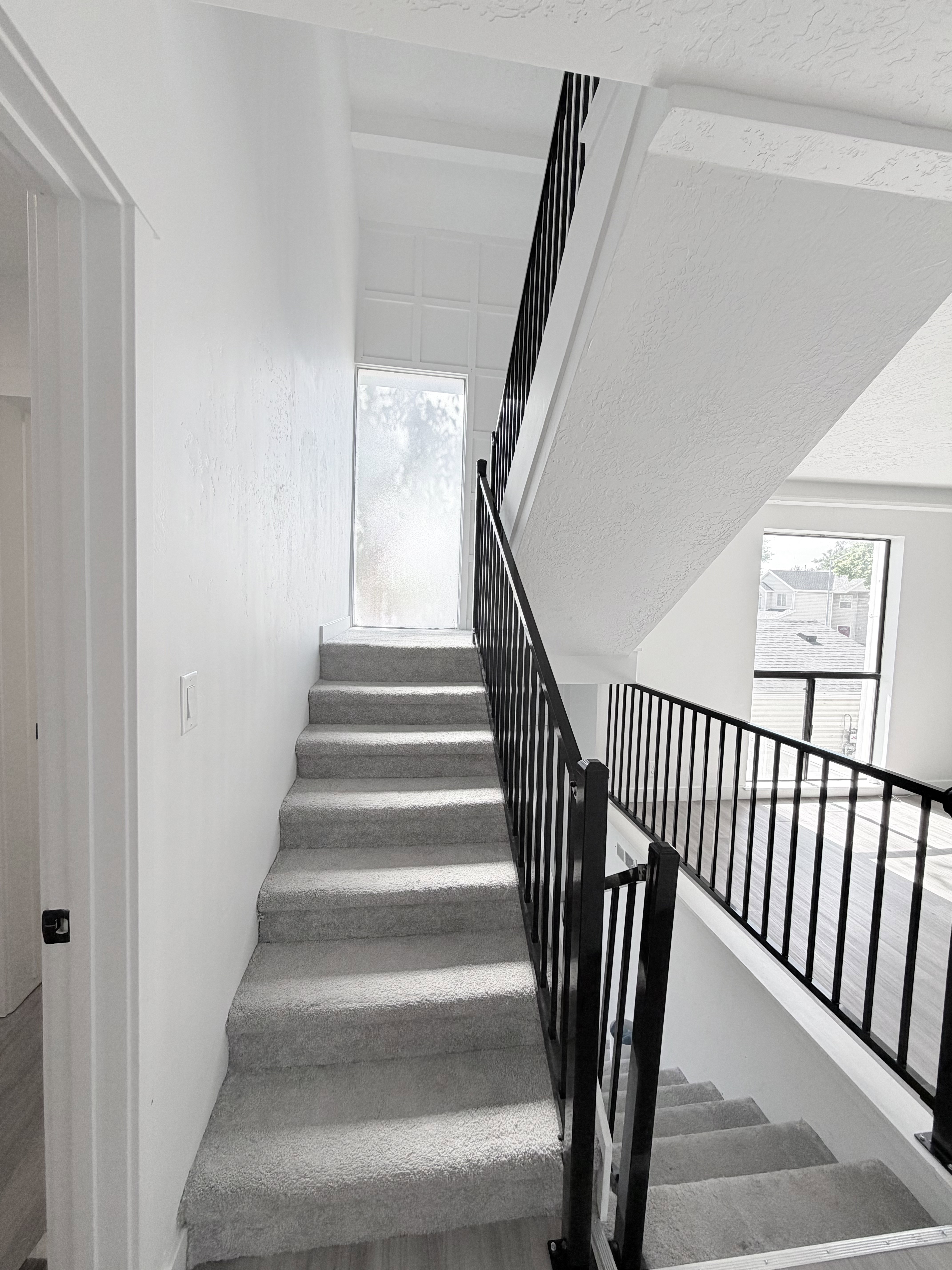 Open-concept staircase featuring light gray carpeting and a contrasting black metal railing