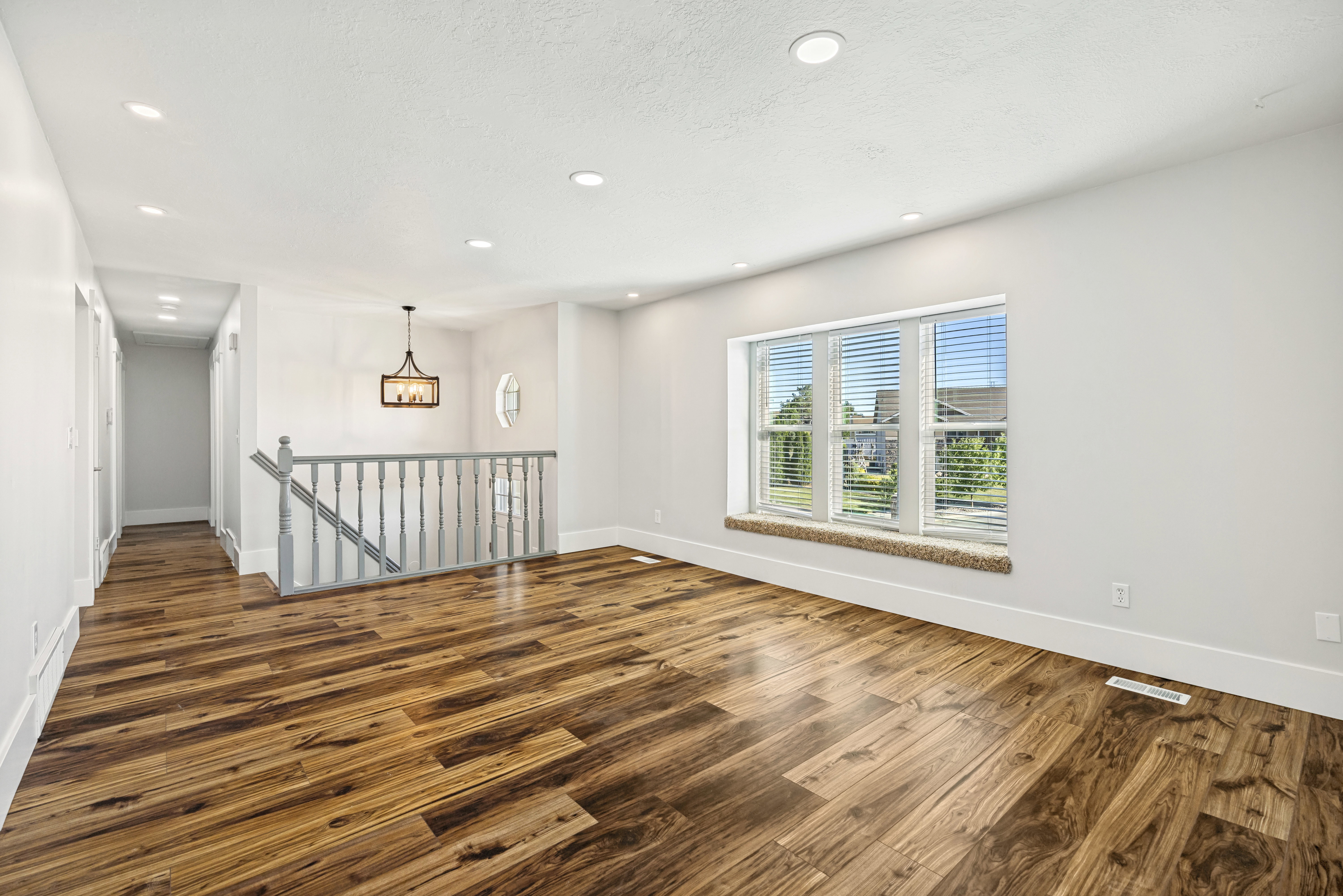 Spacious interior featuring wood-finish flooring, a window with a carpeted sill, recessed lighting, a decorative chandelier, and a white baluster railing