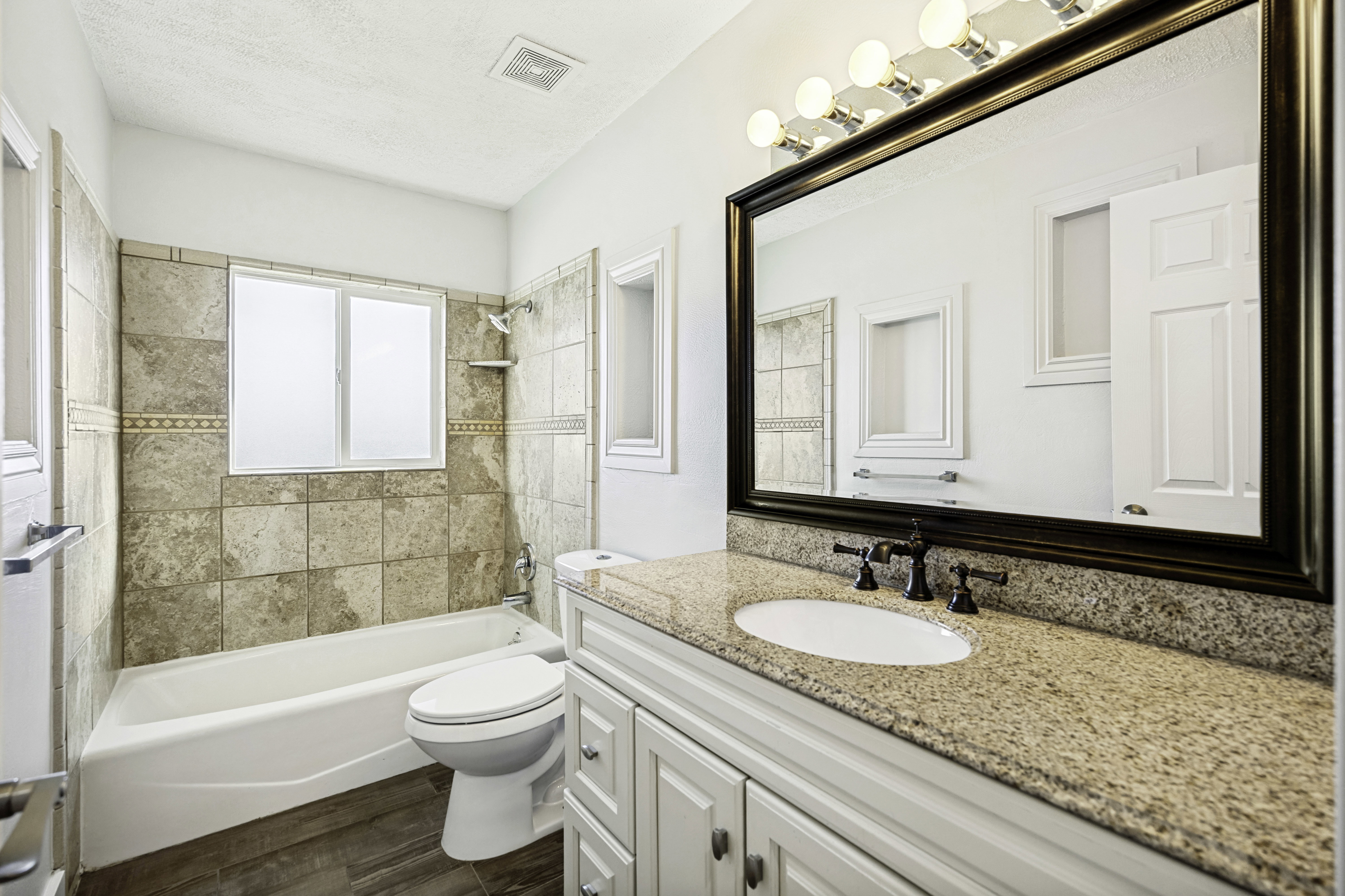 Bathroom featuring a built-in tub with tile surround, a single vanity with a solid surface countertop, white cabinetry, and wood-finish flooring
