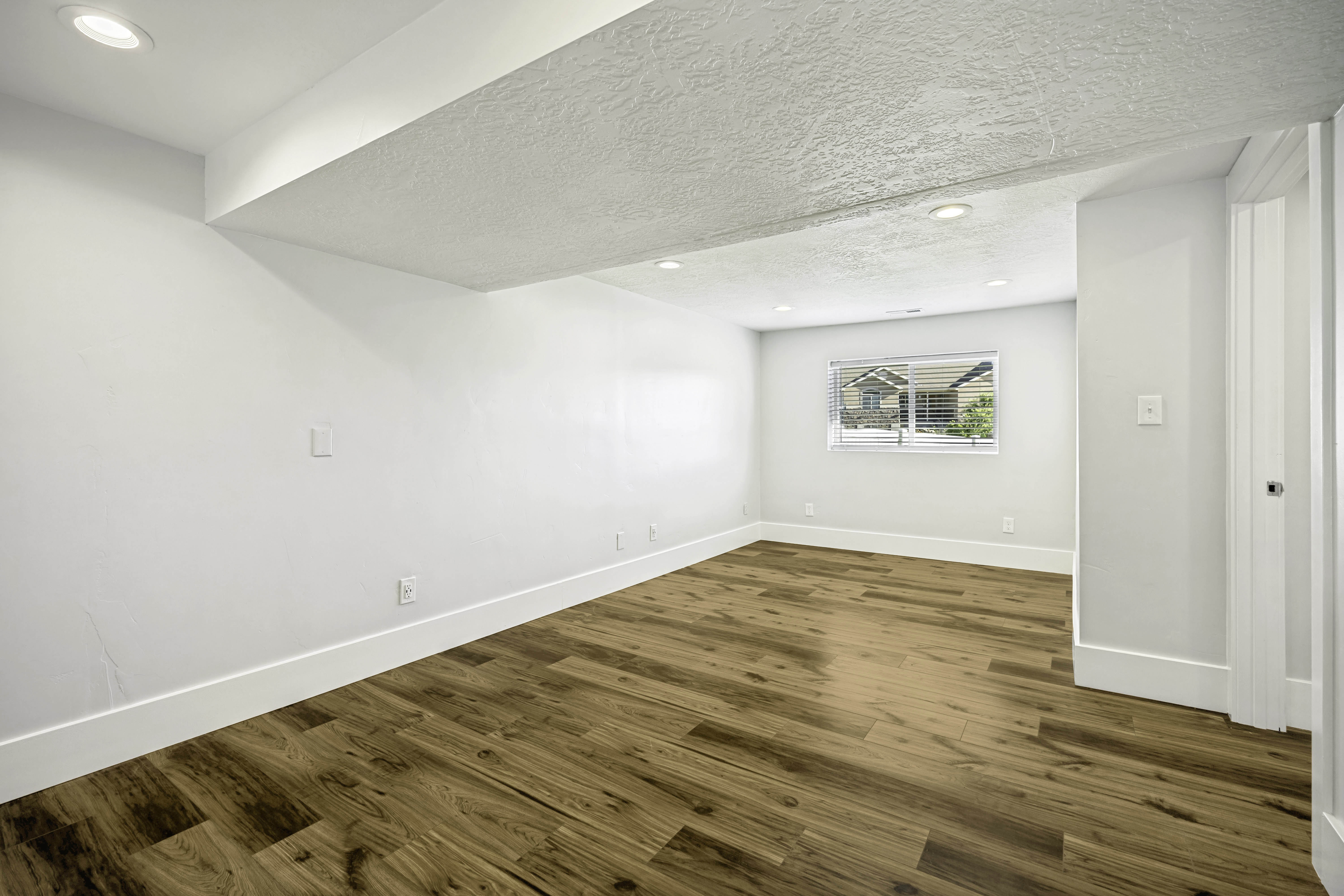 Spacious room featuring wood-finish flooring, recessed lighting, and a window with blinds
