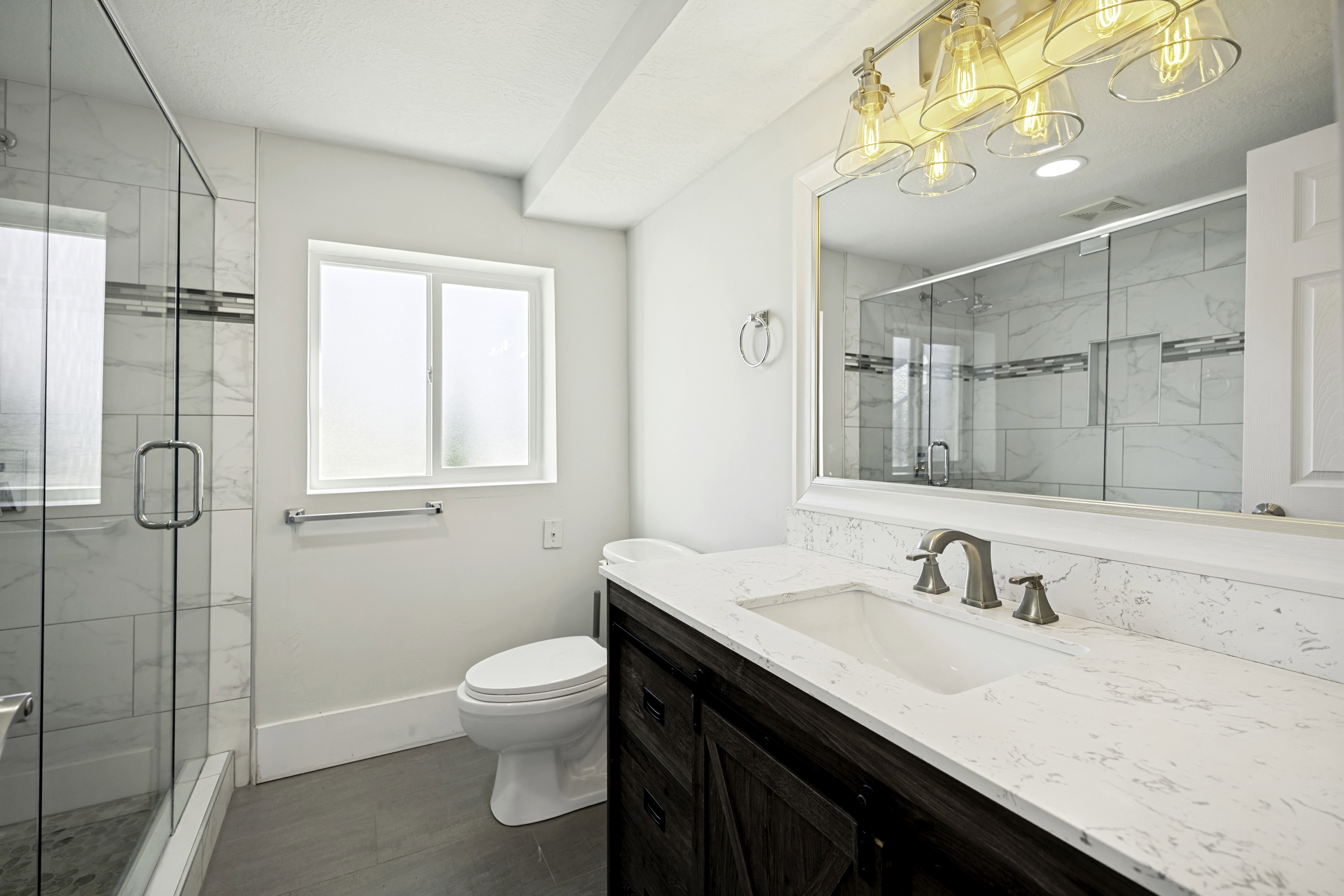 Bathroom featuring a dual-sink vanity with a light-toned countertop, a shower enclosure with glass doors, and a frosted window
