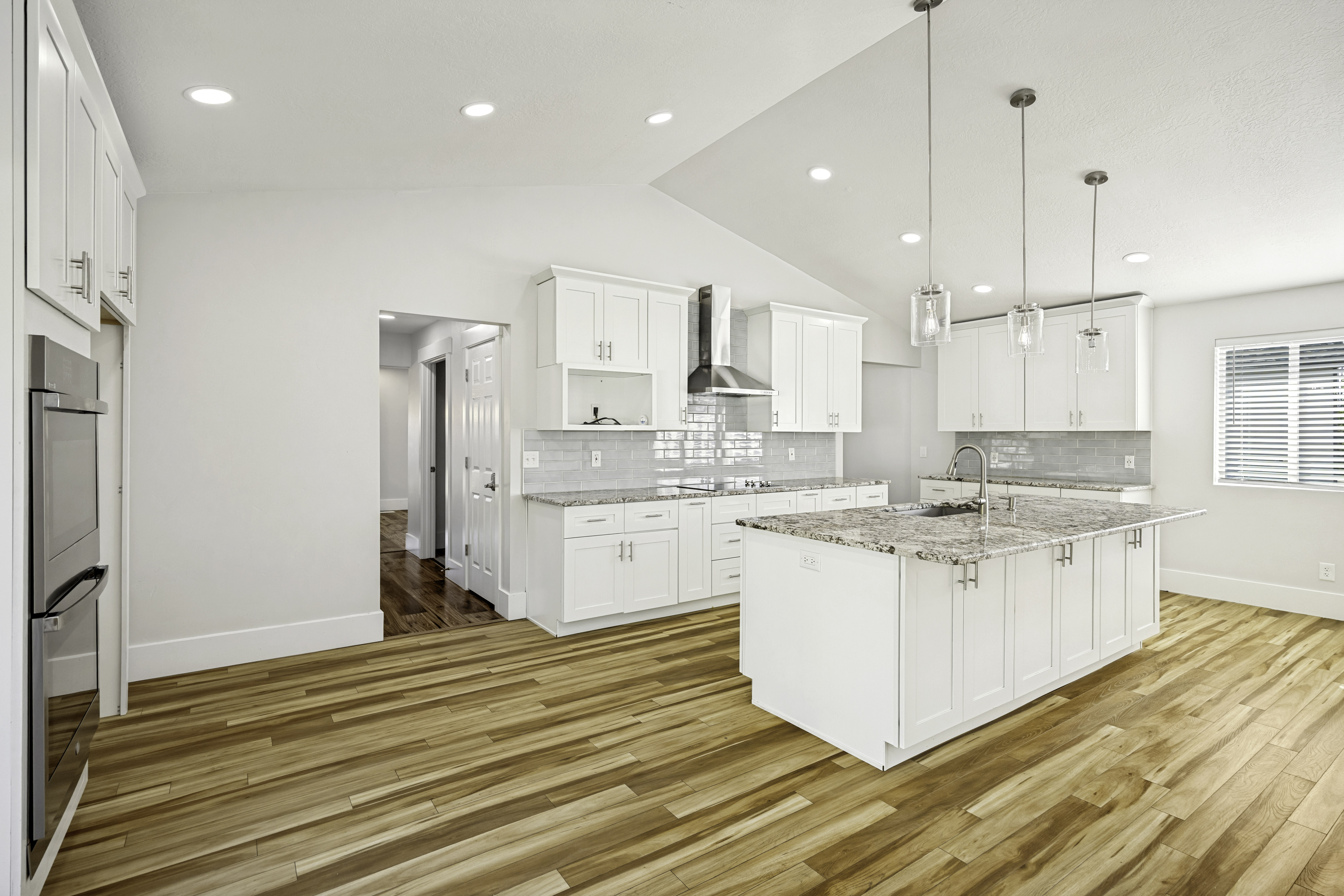 Spacious kitchen featuring an island with a sink, white cabinetry, integrated stainless steel appliances, wood-finish flooring, and recessed lighting