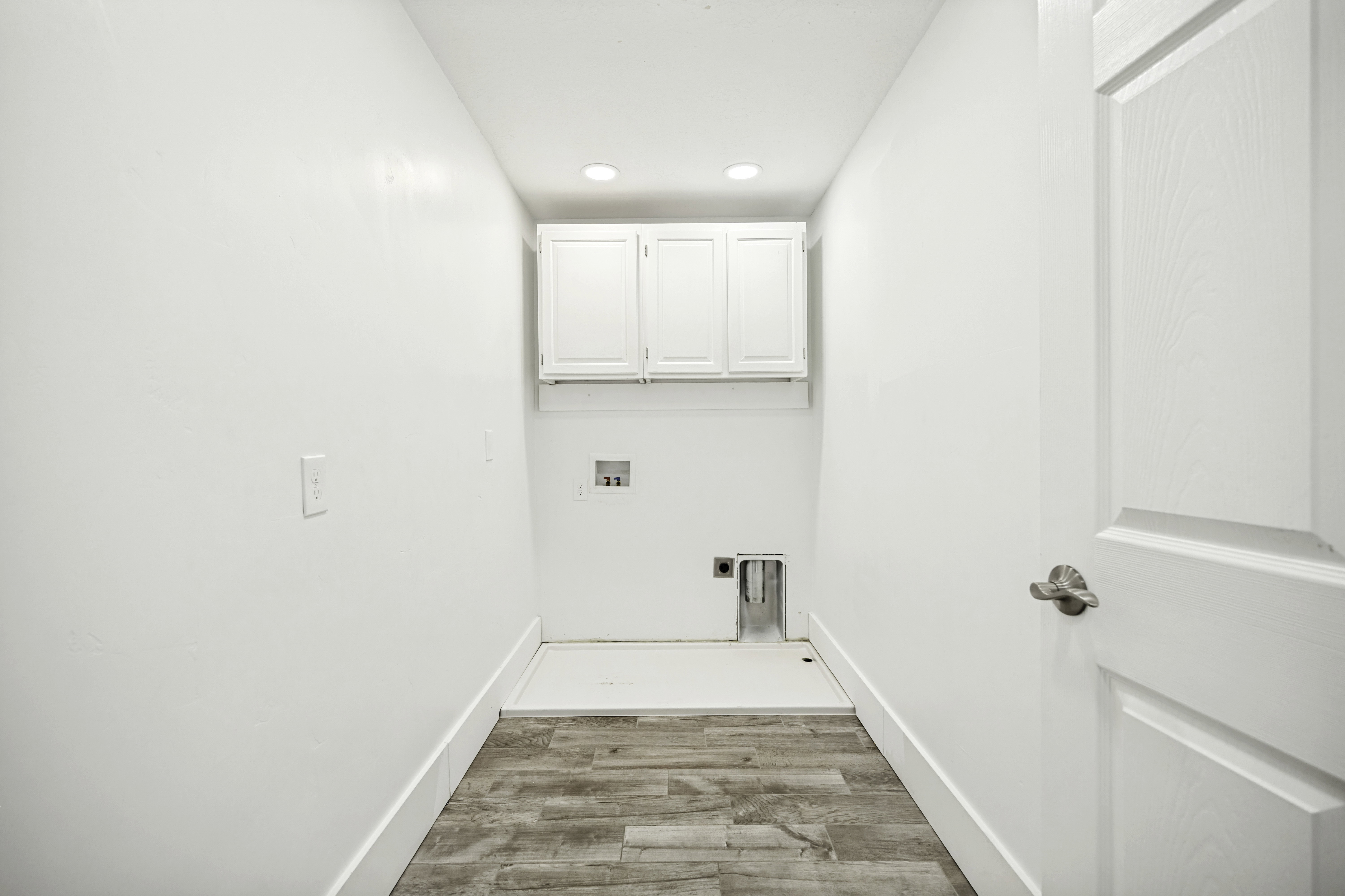 Laundry area featuring wood-finish flooring, white cabinetry, recessed lighting, and a paneled door with brushed nickel hardware