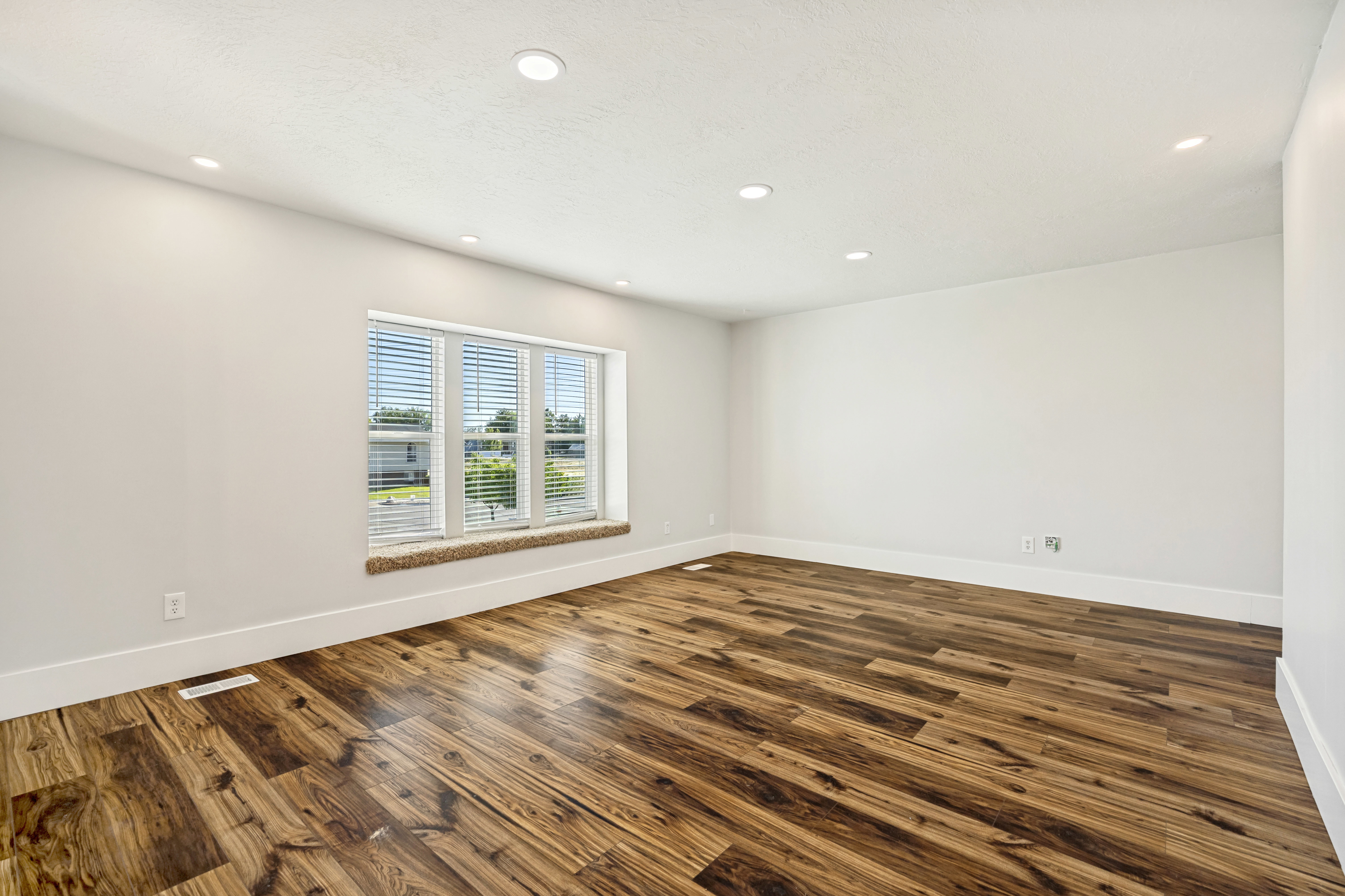 Spacious room featuring wood-finish flooring, recessed lighting, and a large window with blinds