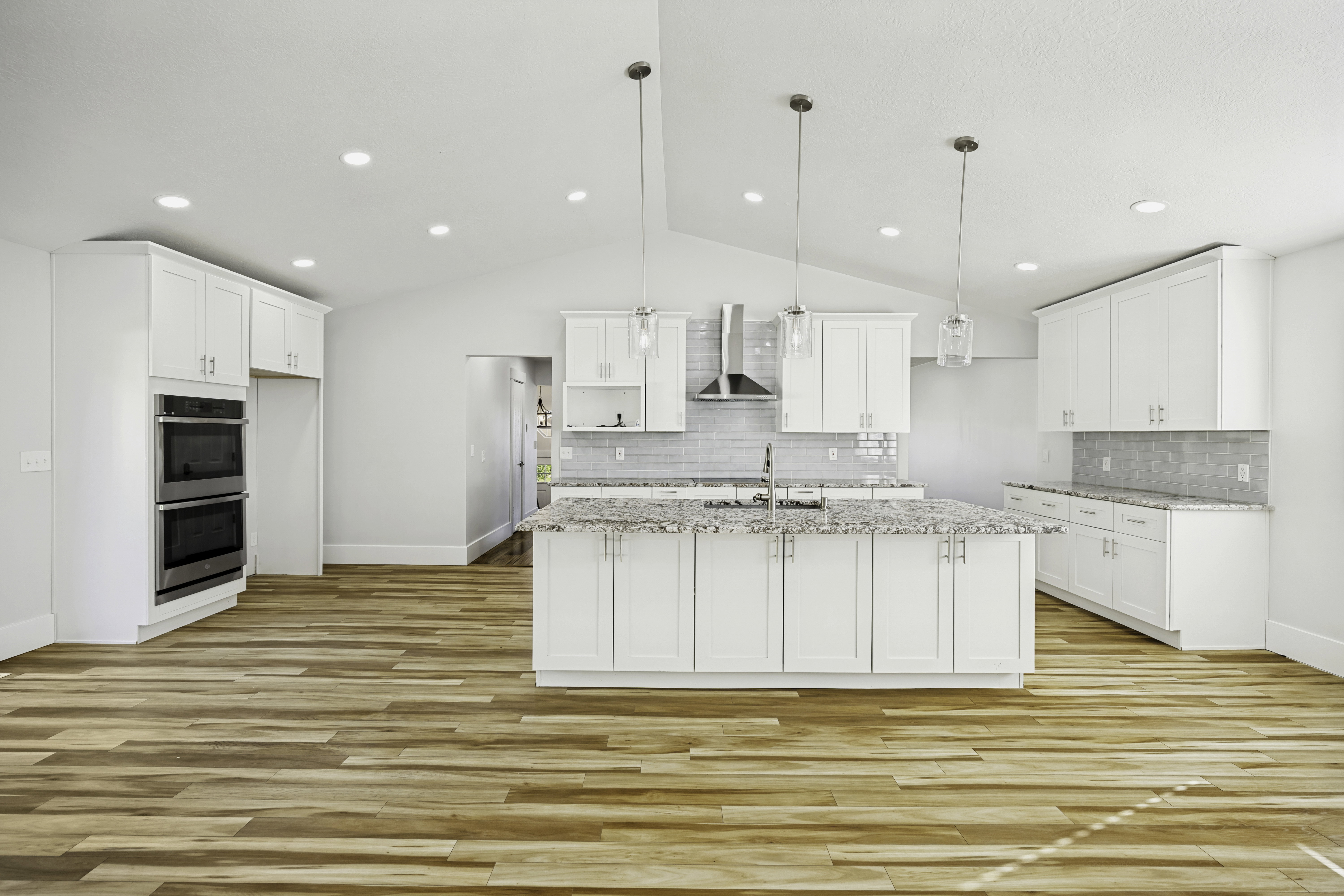 Spacious kitchen featuring an expansive center island with seating, pendant lighting, wood-finish flooring, white cabinetry, and stainless steel double ovens