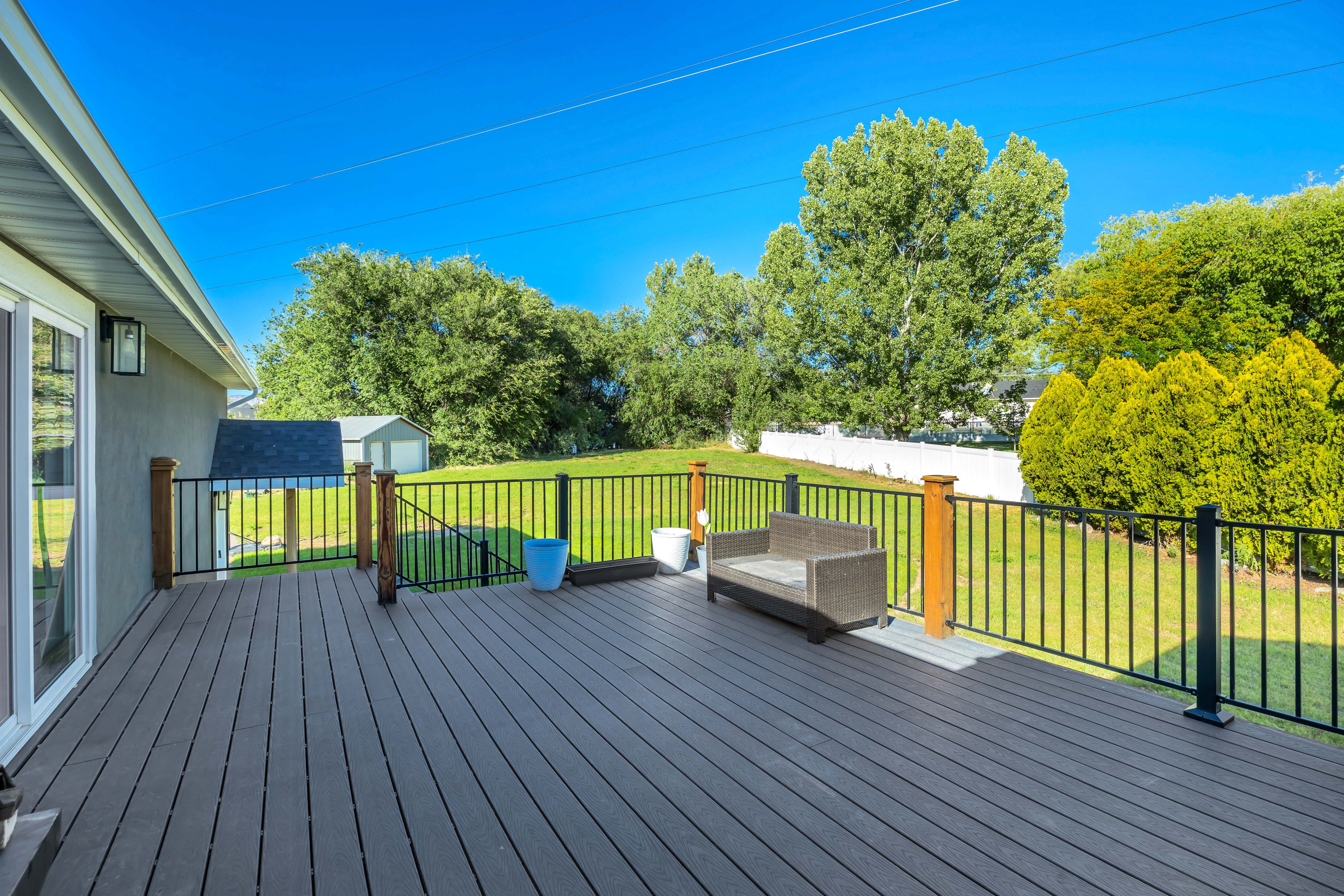 Spacious composite deck with black metal railings and natural wood posts, overlooking a large grassy area with mature landscaping