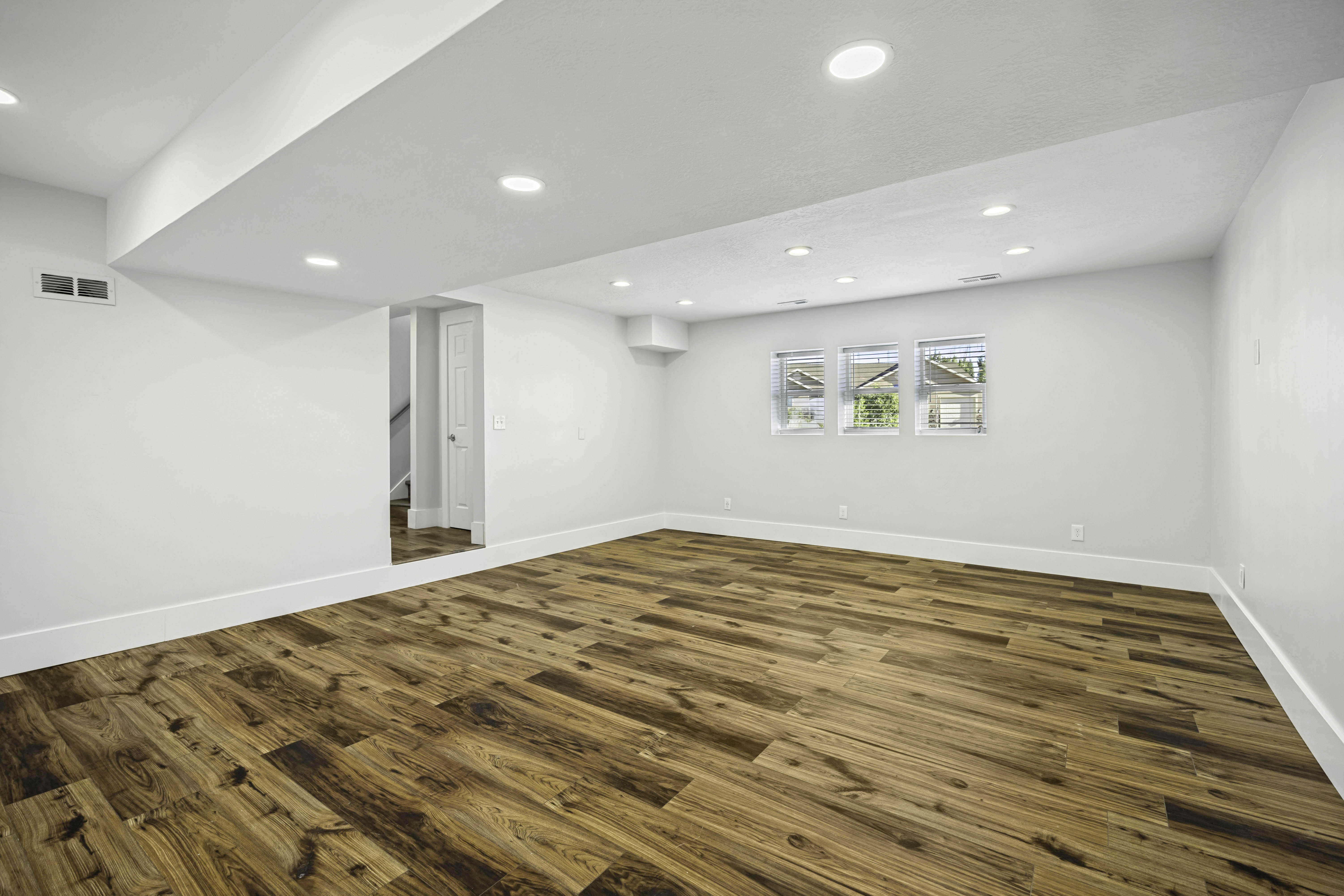 Spacious room featuring wood-finish flooring, white walls, recessed lighting, and three windows