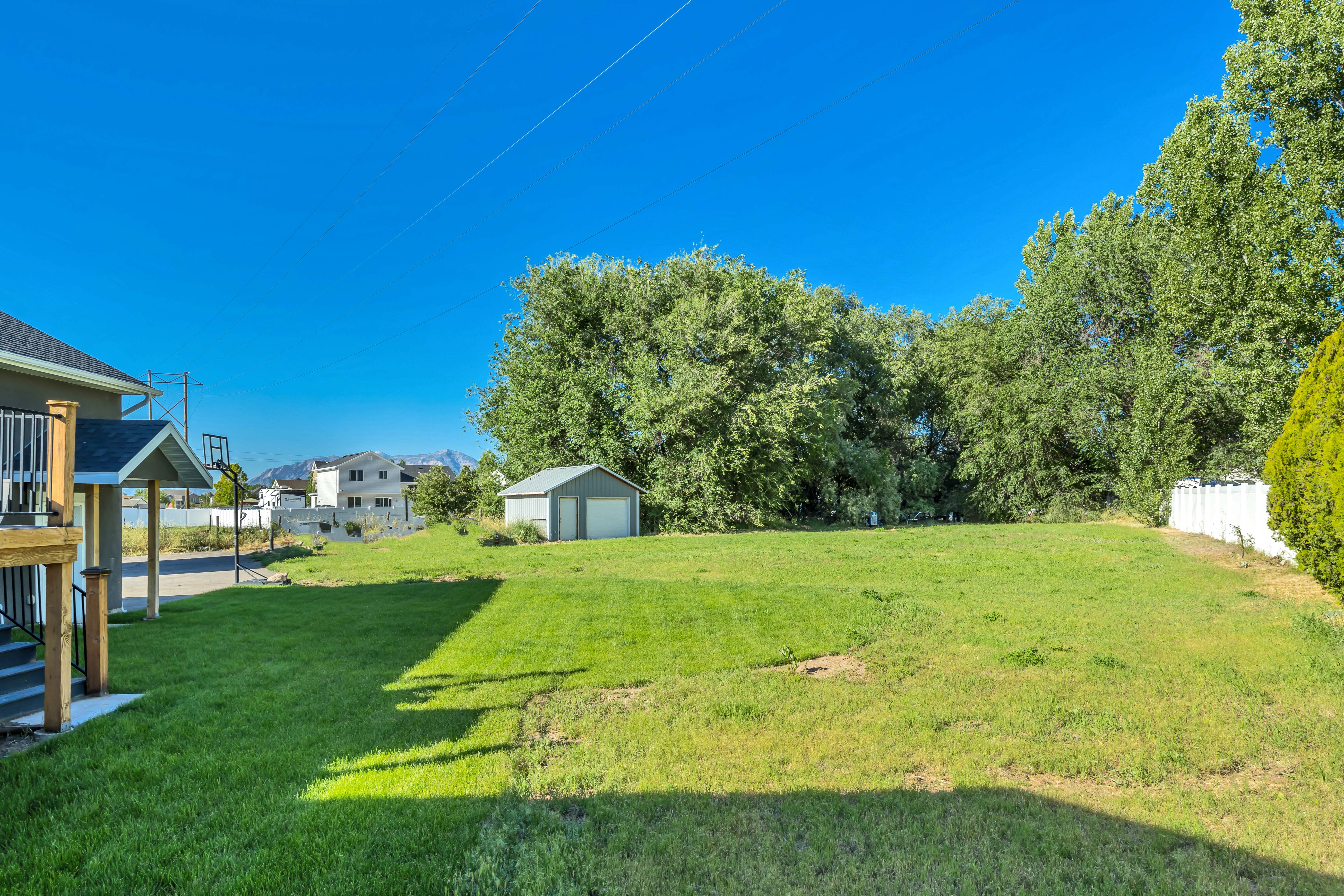 Expansive green lawn featuring a detached shed with a roll-up garage door, mature perimeter trees, and a partial privacy fence