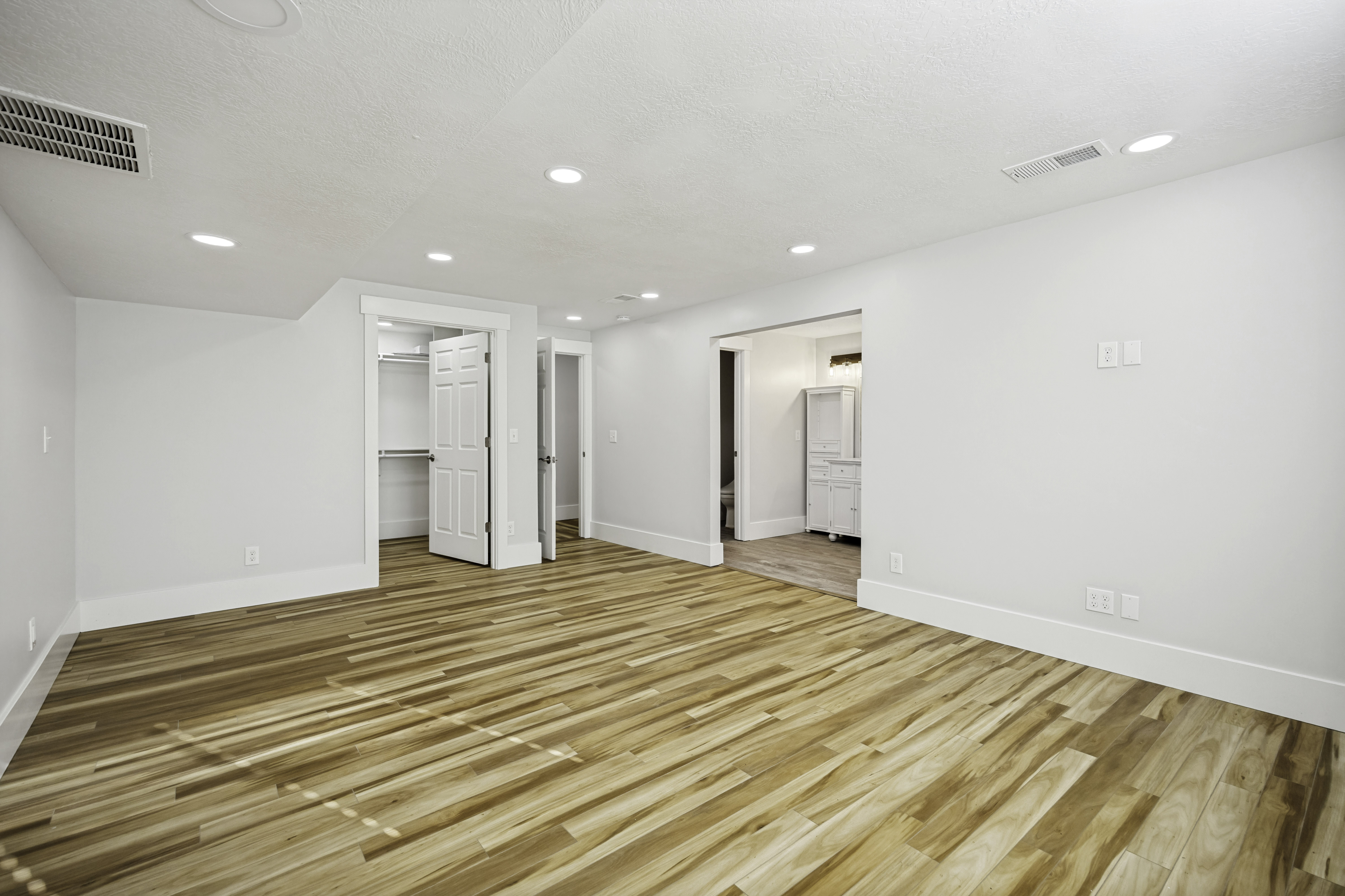 Spacious interior room featuring wood-finish flooring, white walls, and recessed lighting
