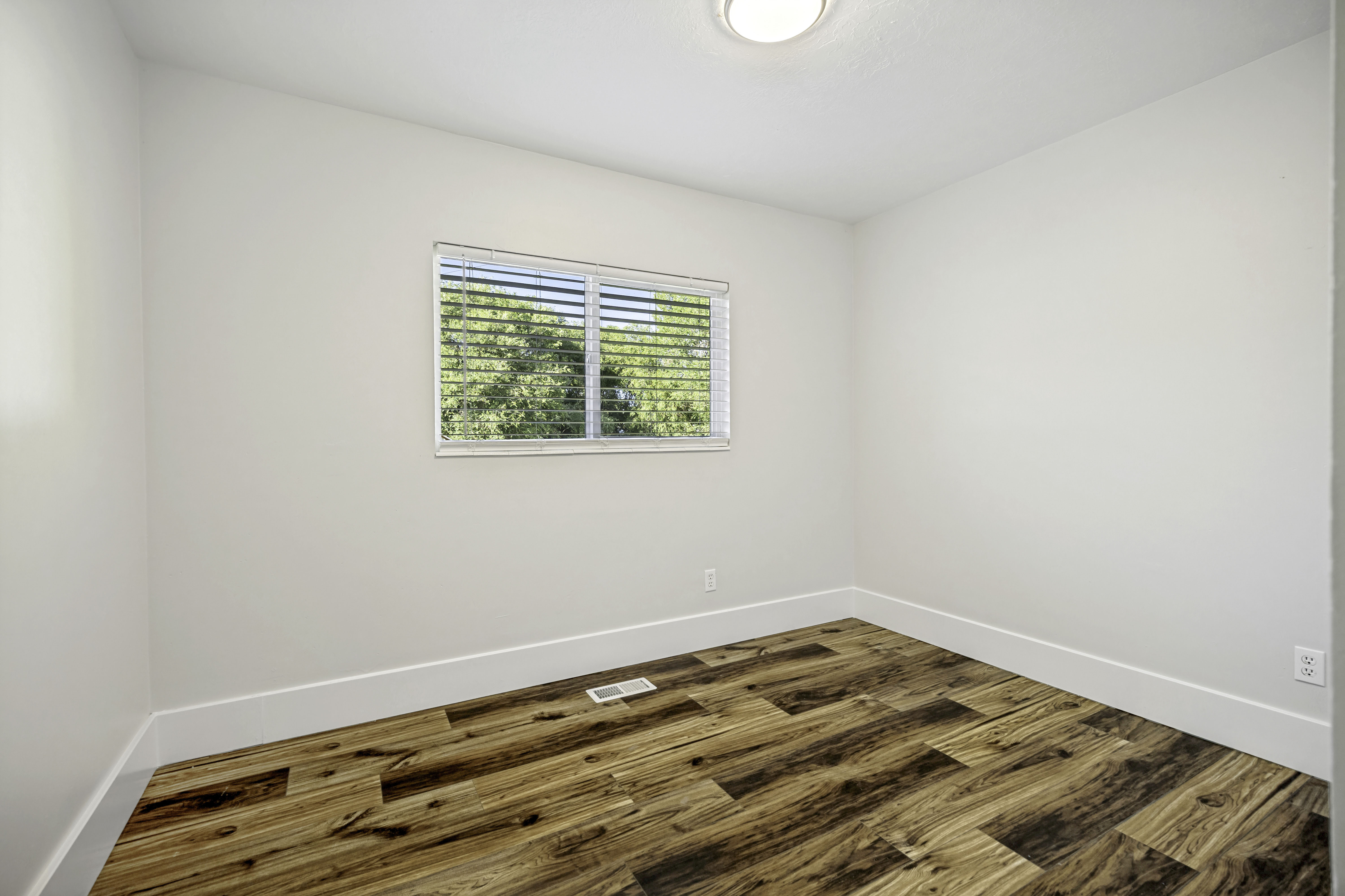 Interior room featuring wood-finish flooring, white baseboards, and a window with blinds
