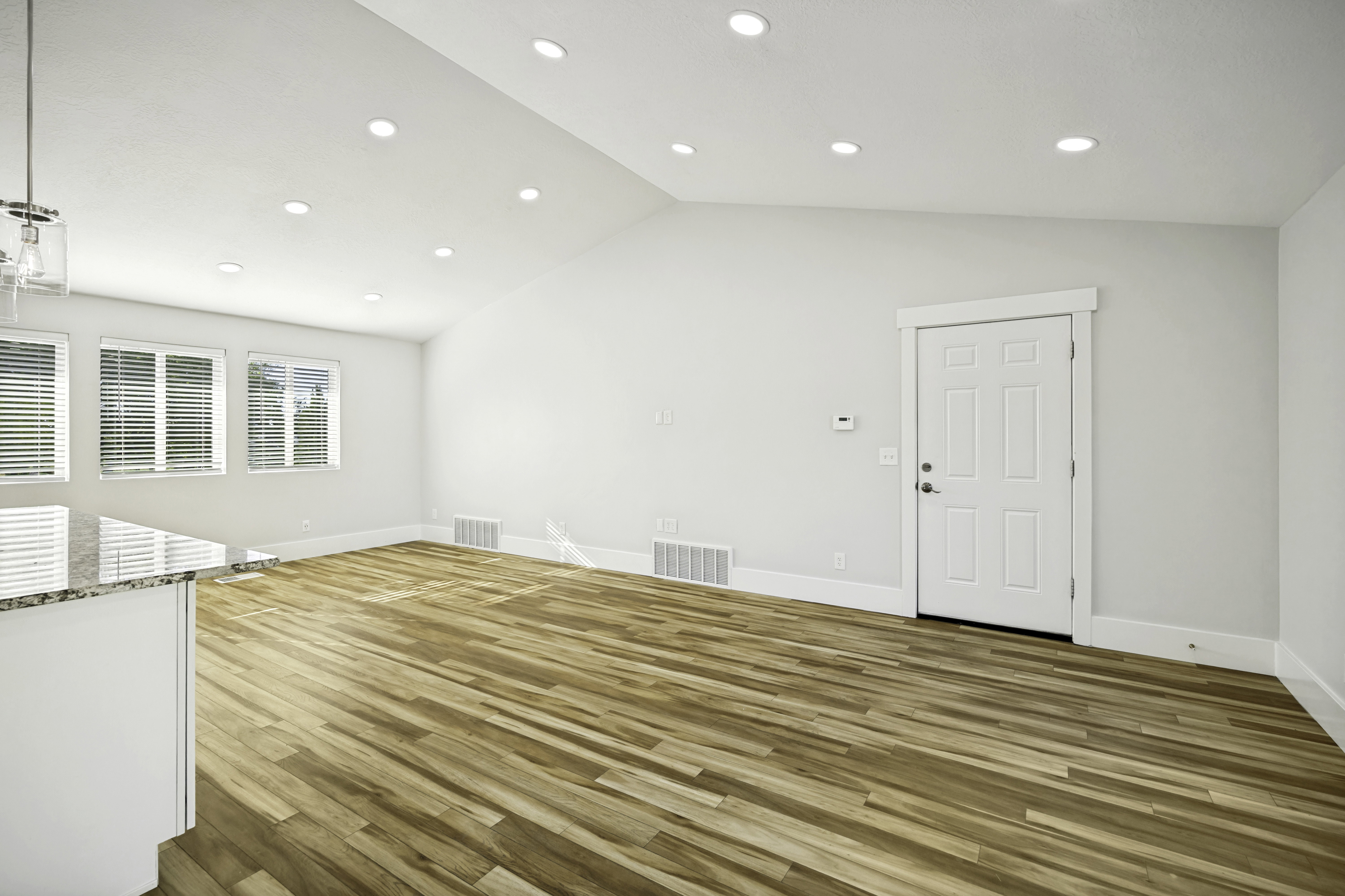 Bright interior space featuring wood-finish flooring, multiple windows with blinds, a white paneled door, and recessed lighting
