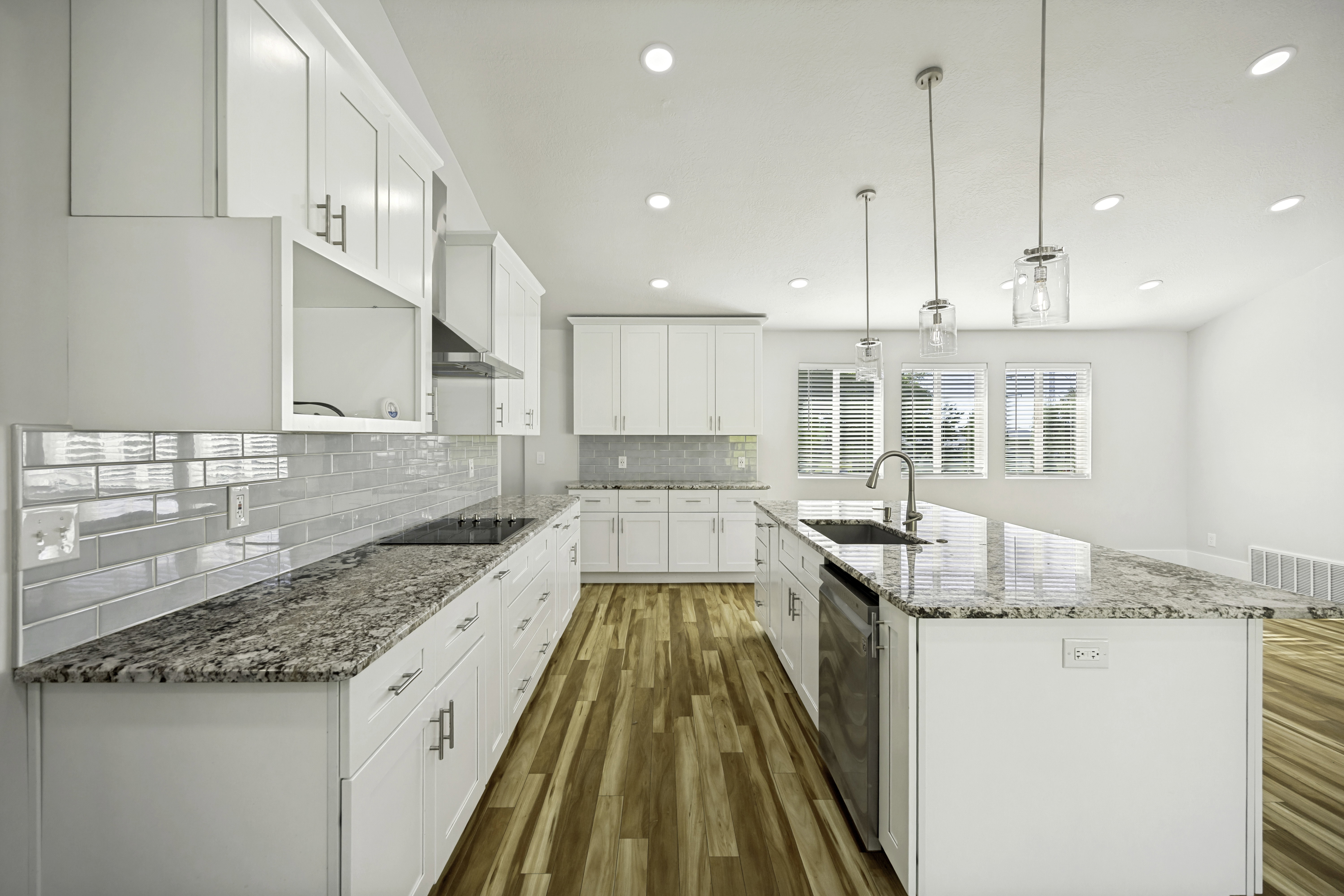 Modern kitchen featuring white cabinetry, a large center island with a stainless steel sink, granite countertops, and wood-finish flooring