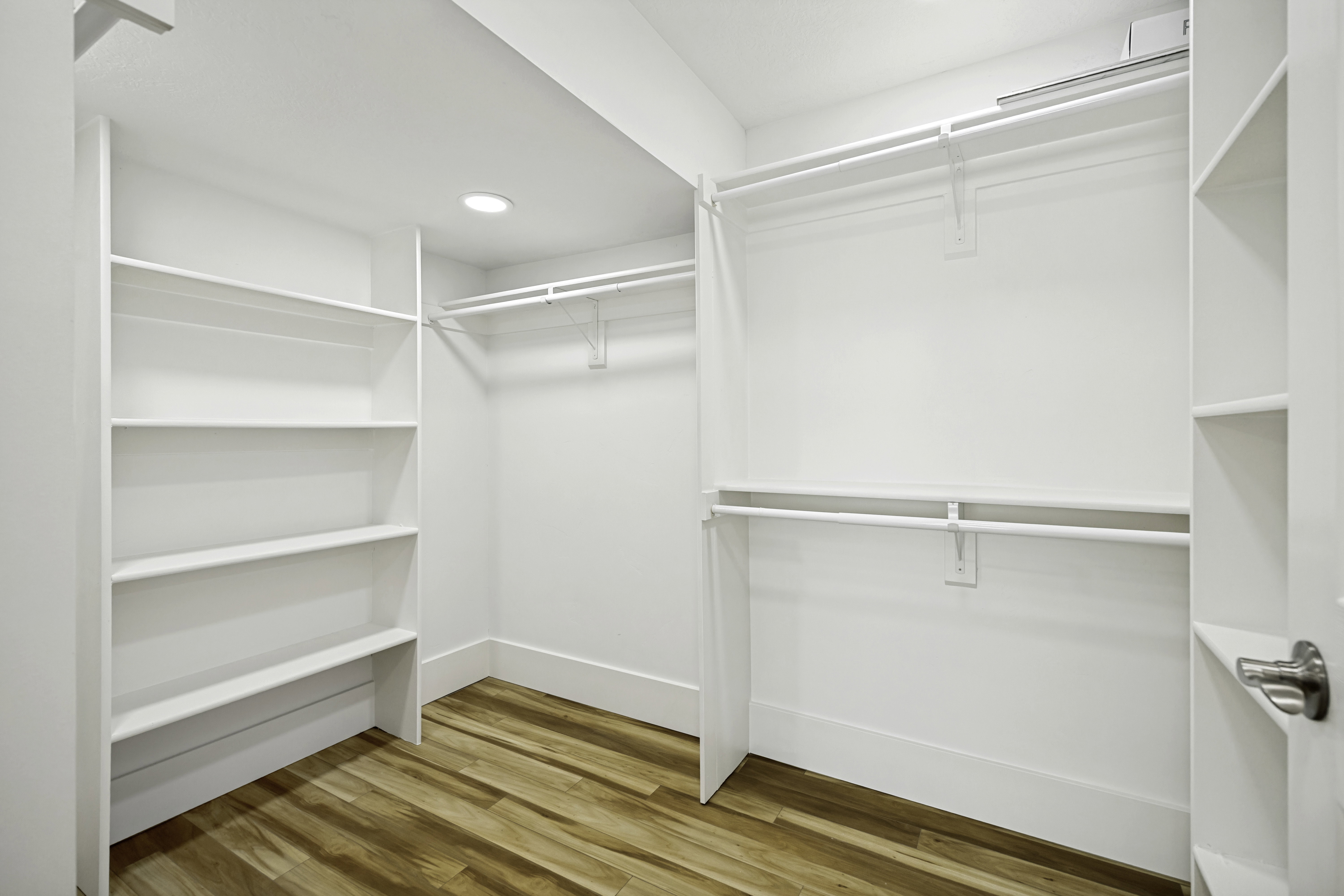 Walk-in closet featuring wood-finish flooring, recessed lighting, white built-in shelving, and white hanging rods