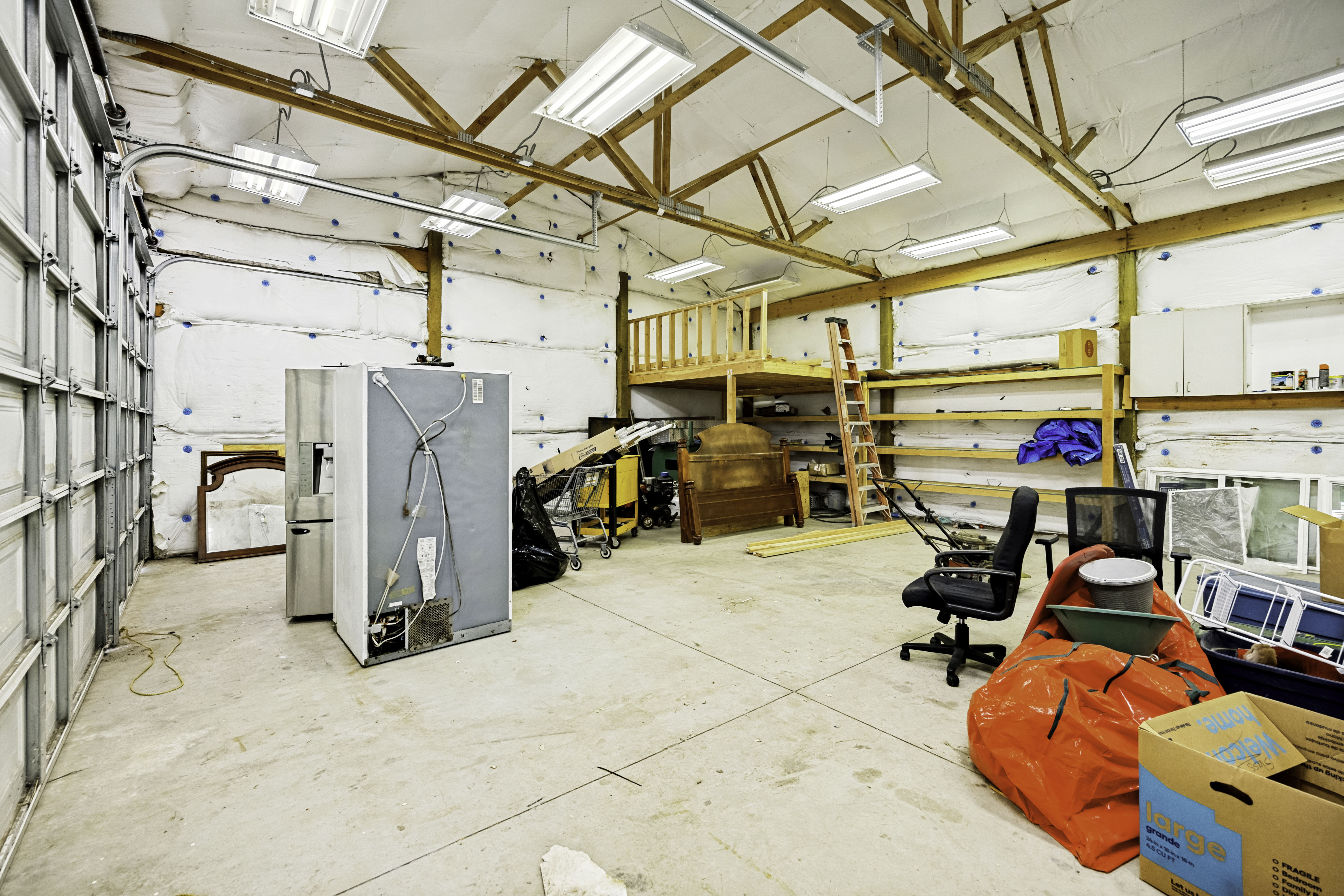 Spacious garage interior featuring high ceilings with exposed wood beams and fluorescent lighting