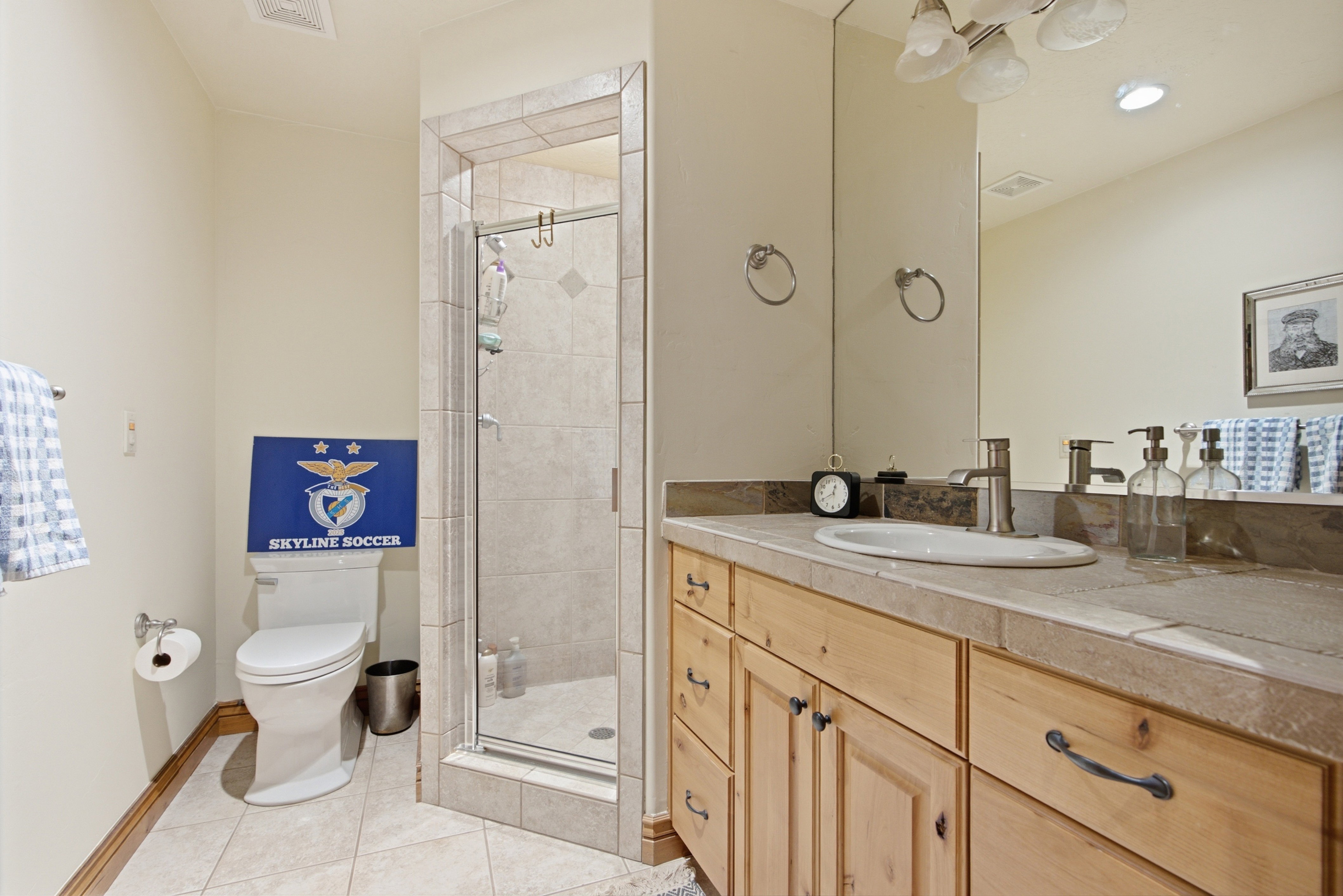Bathroom featuring a light wood-finish vanity with an undermount sink, tiled countertop, and an expansive mirror