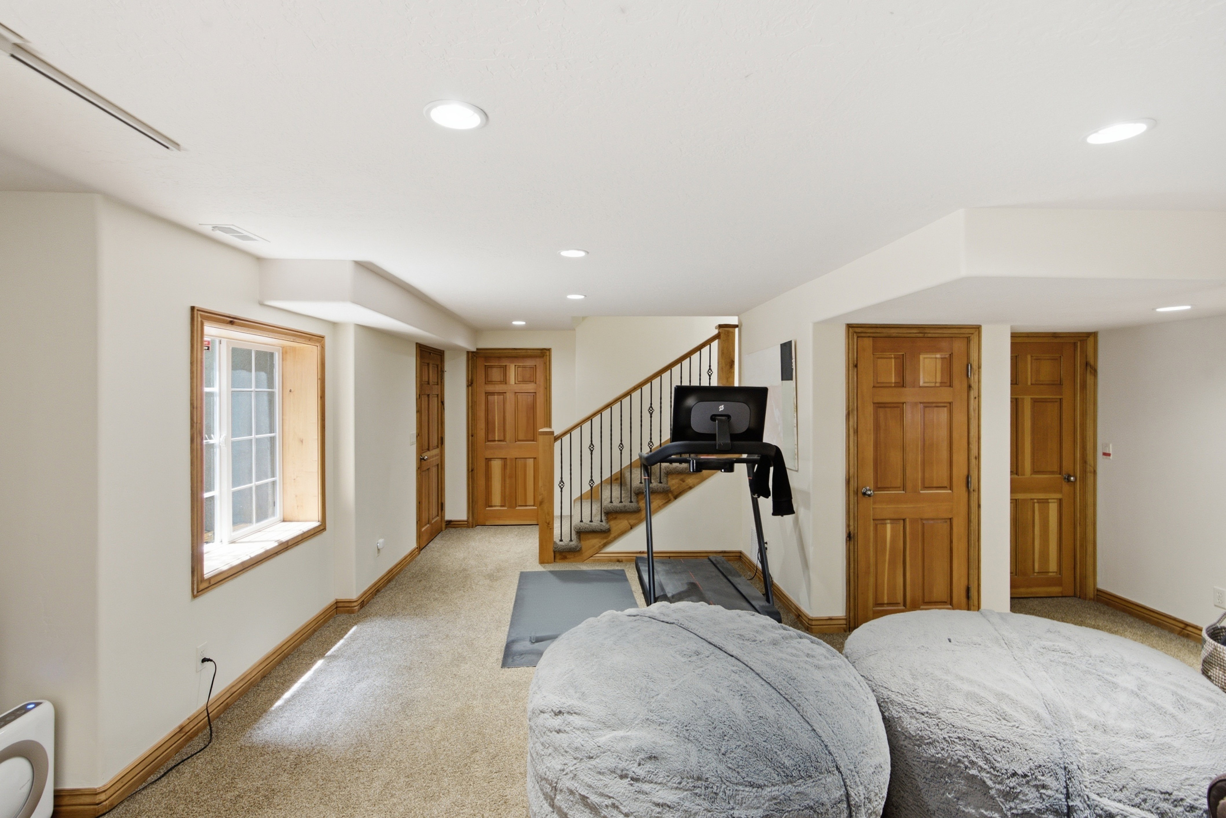 Finished lower level featuring recessed lighting, a staircase with wrought iron balusters, light wood-finish doors, and a window with wood trim