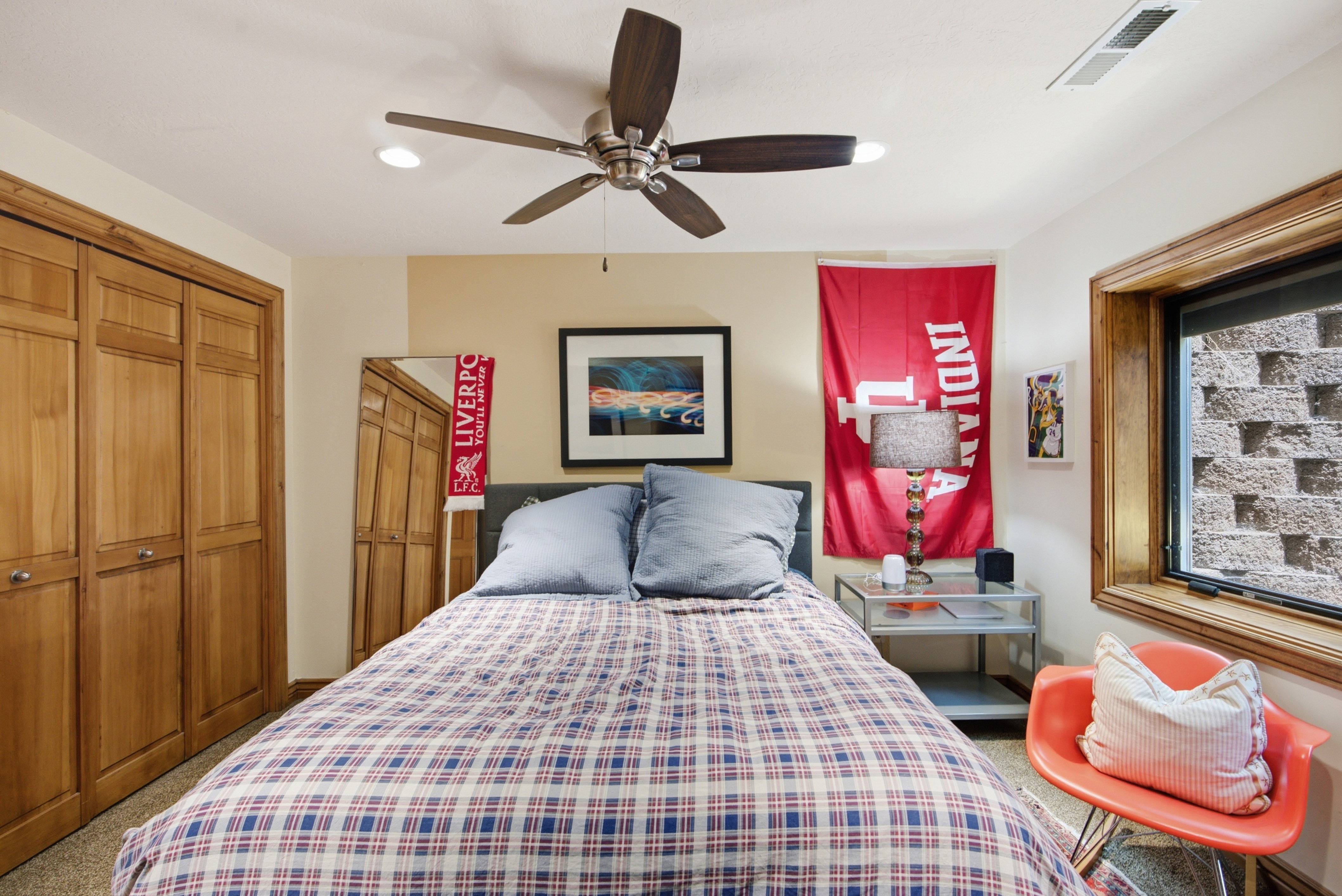 Recessed lighting illuminates this room featuring wood-finish bi-fold closet doors, a wood-trimmed window, and a ceiling fan with integrated lighting