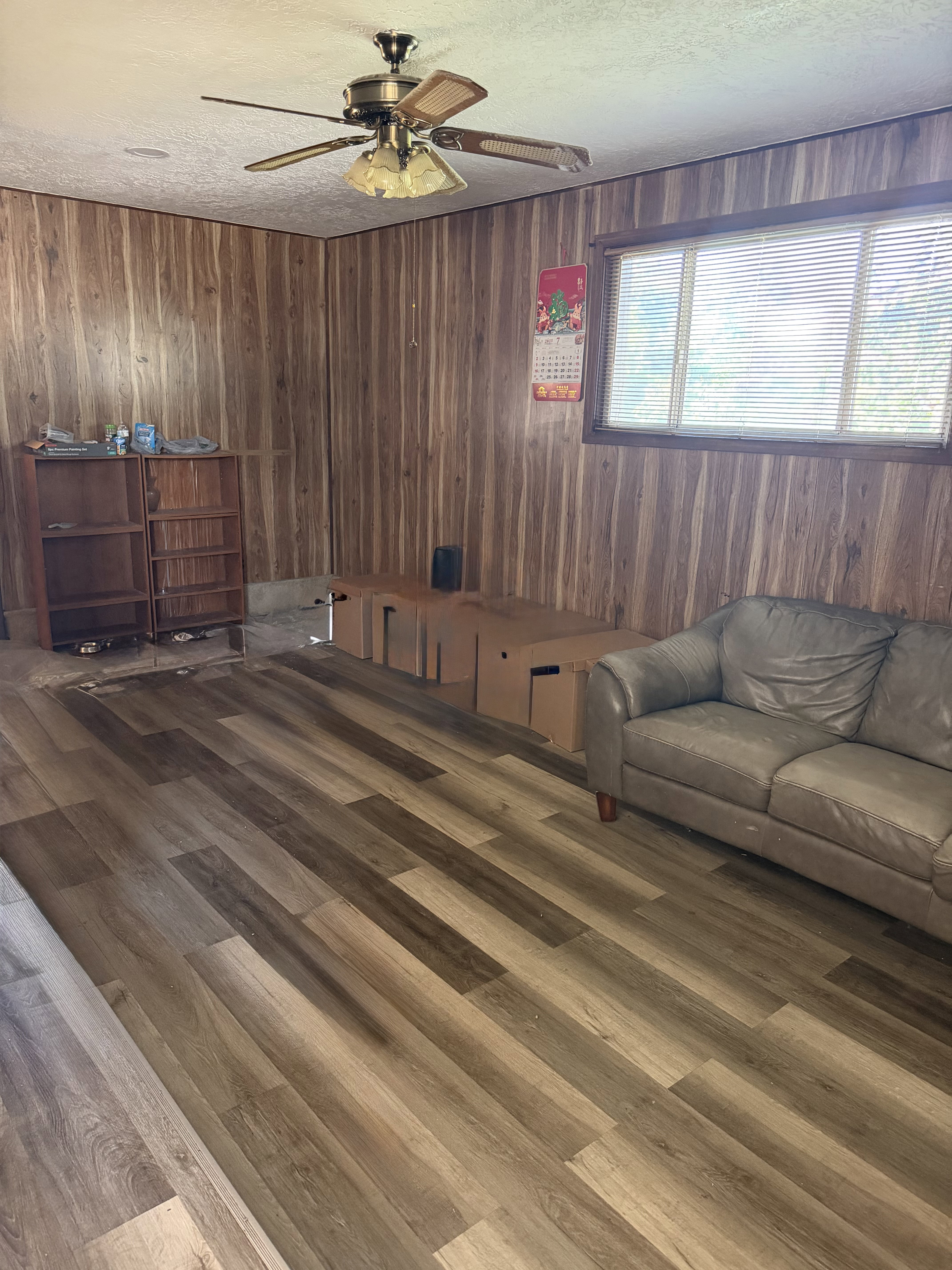 Spacious room featuring wood-finish paneling, a multi-pane window with blinds, and a ceiling fan with integrated lighting