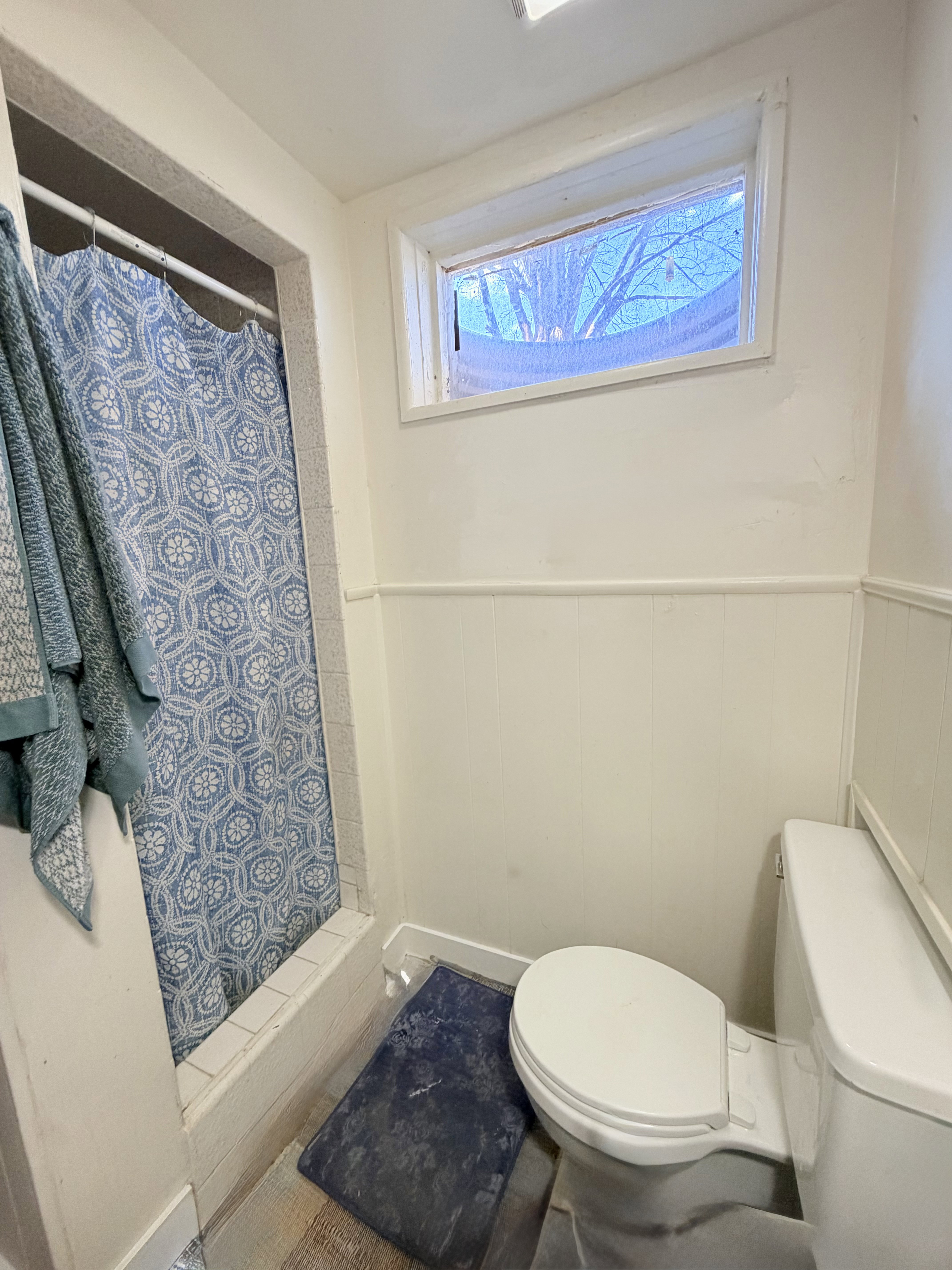 Bathroom featuring a white toilet, wainscoting, and a window with trim