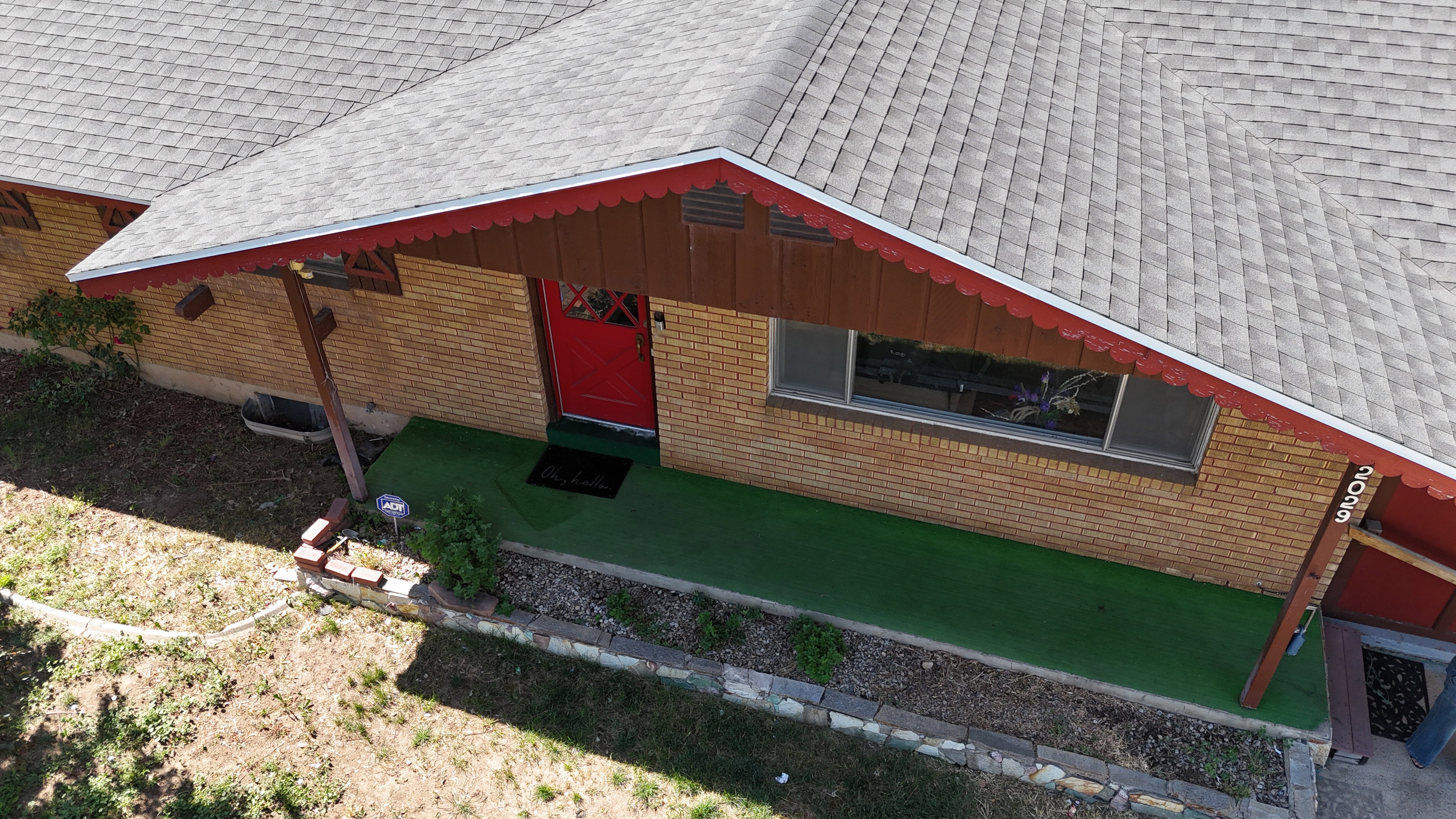 Brick exterior featuring a red entry door, a covered porch with decorative wood trim, and a window with a stone sill