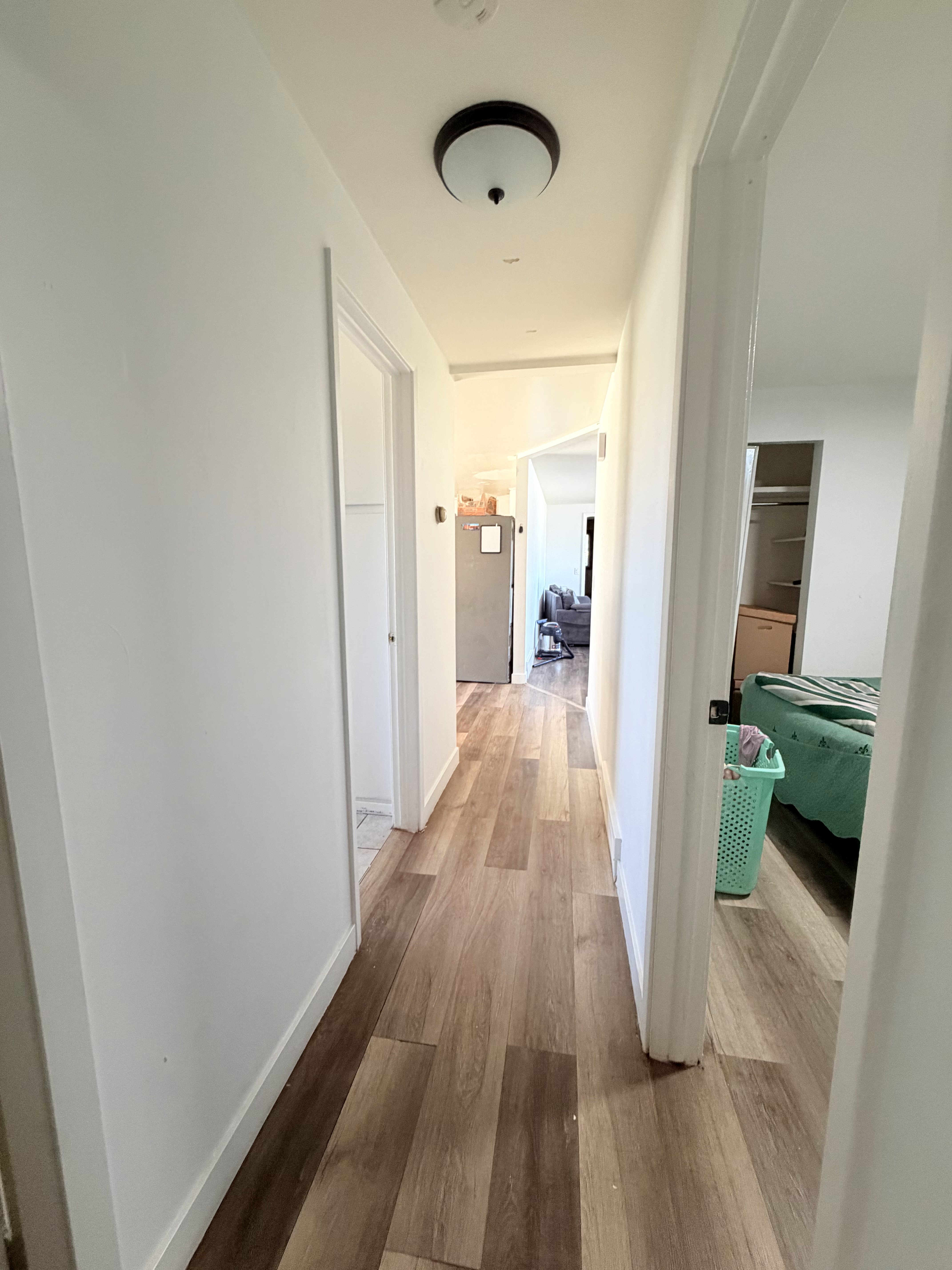 Hallway featuring wood-finish flooring, white baseboards, and a flush-mount ceiling light fixture