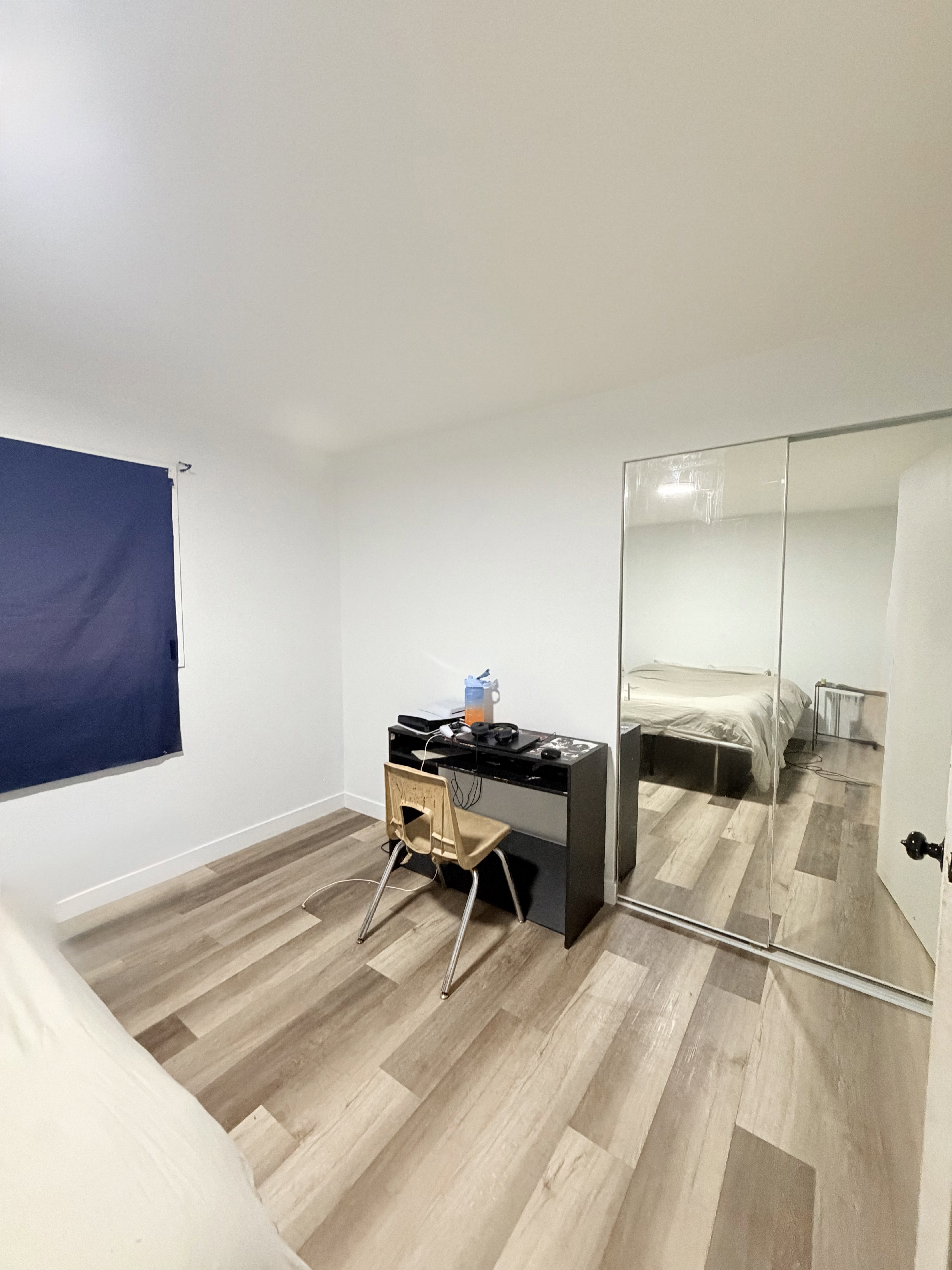 Room featuring wood-finish flooring, white walls, and a window with a blue roller shade