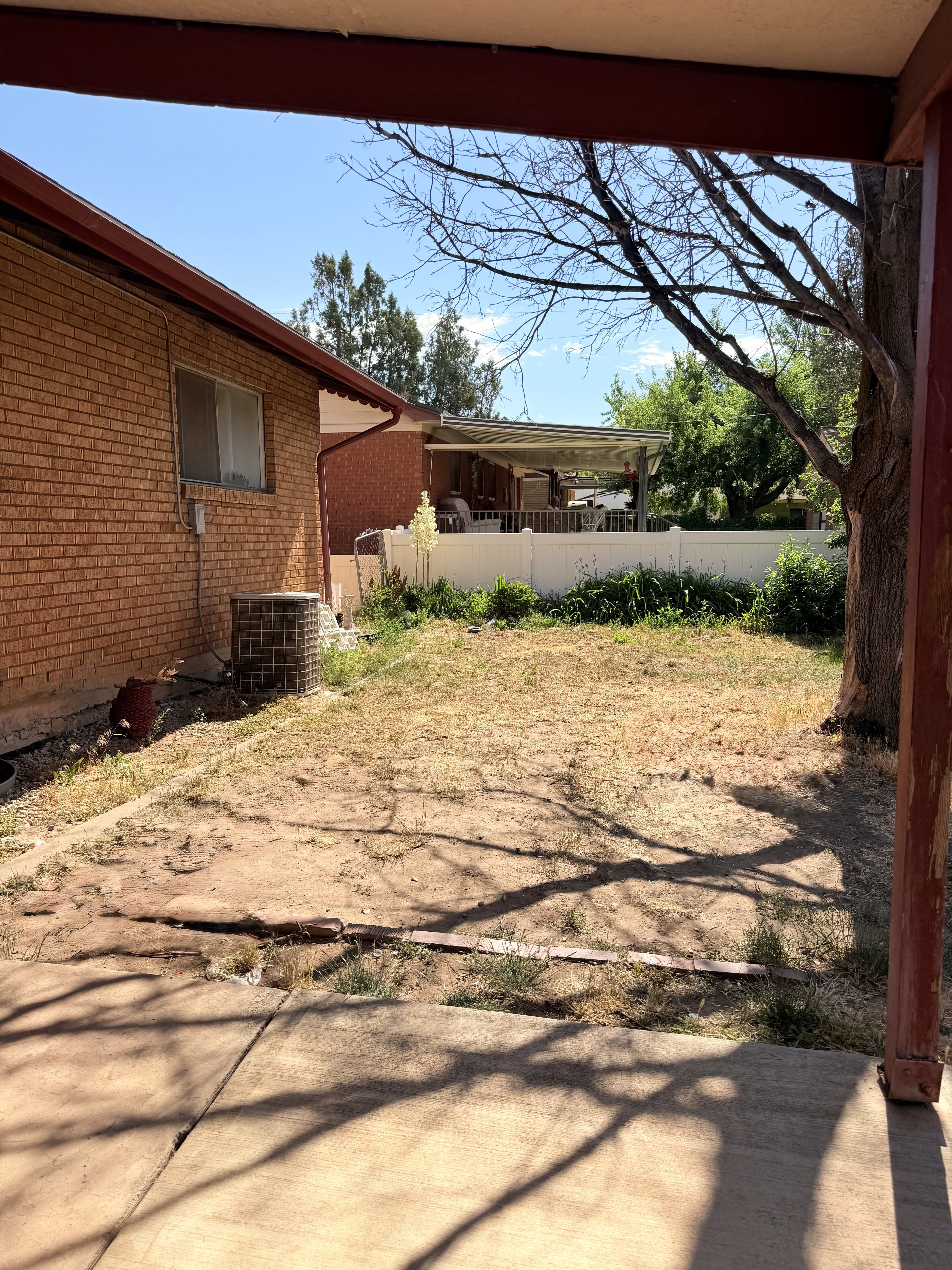 Spacious backyard with a covered patio, brick exterior, and mature trees