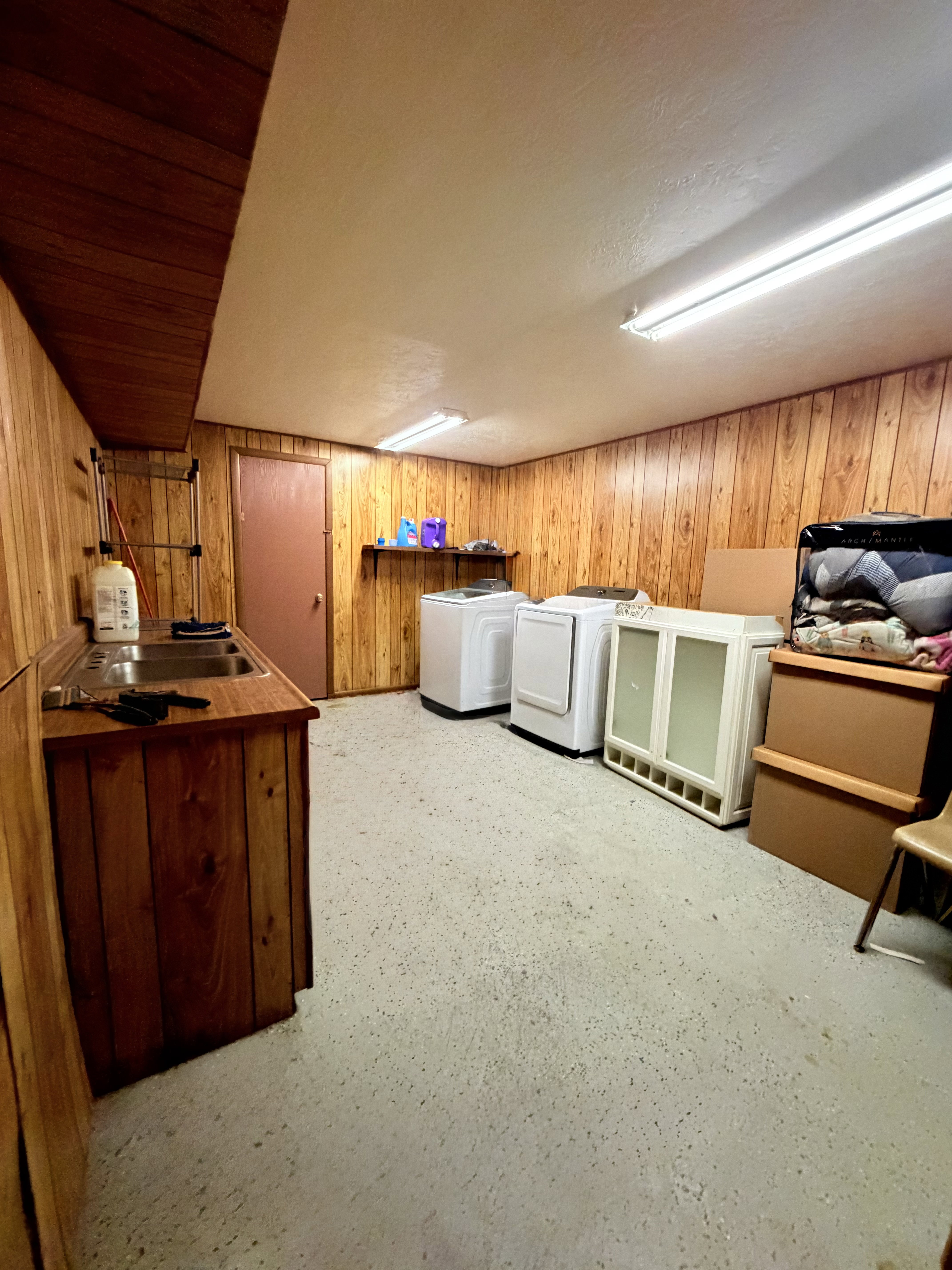 Utility room featuring wood paneling, a built-in sink with cabinetry, and concrete flooring