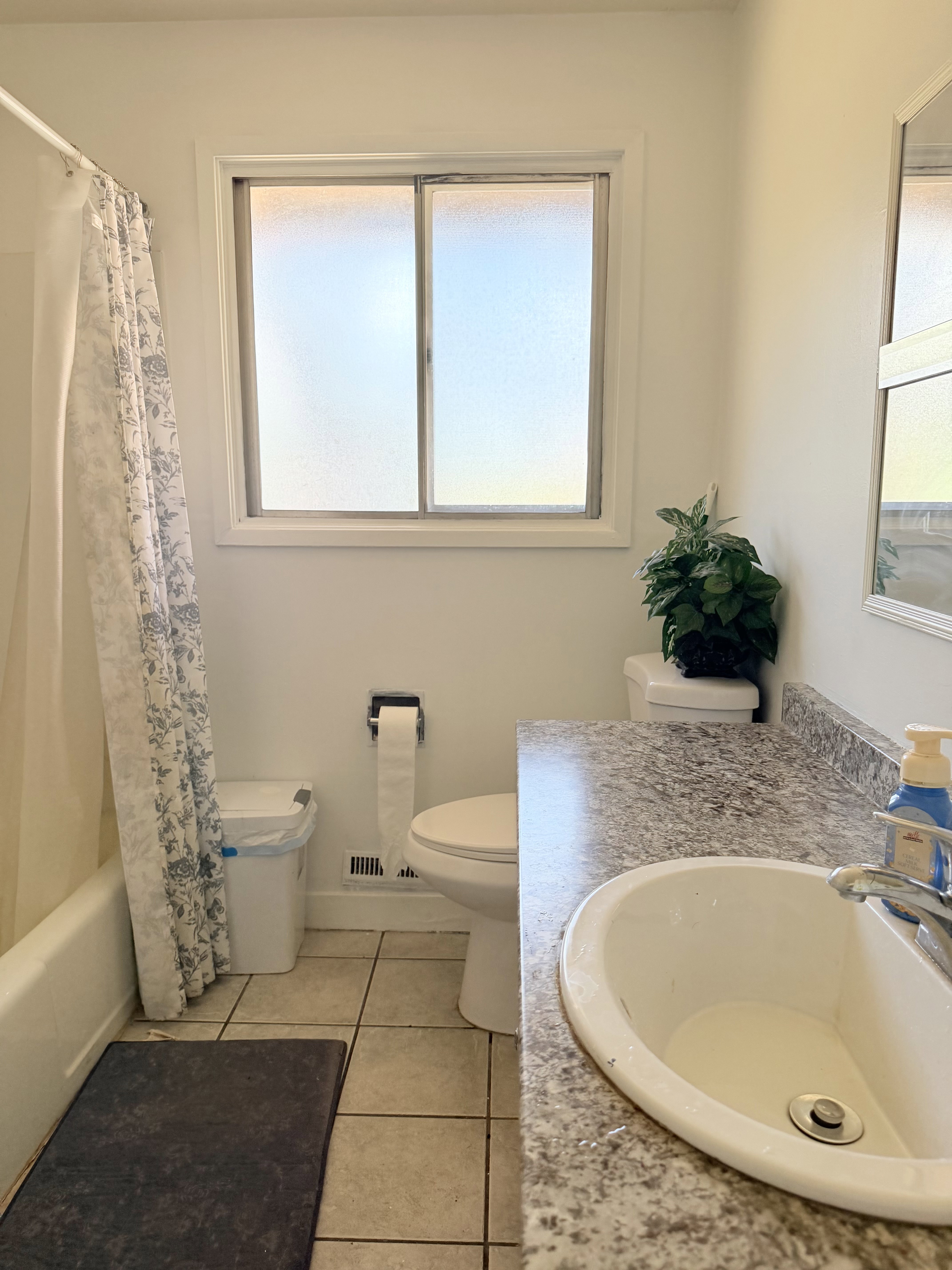 Bathroom featuring a tiled floor, white bathtub with shower, white toilet, and a vanity with a laminate countertop and integrated sink
