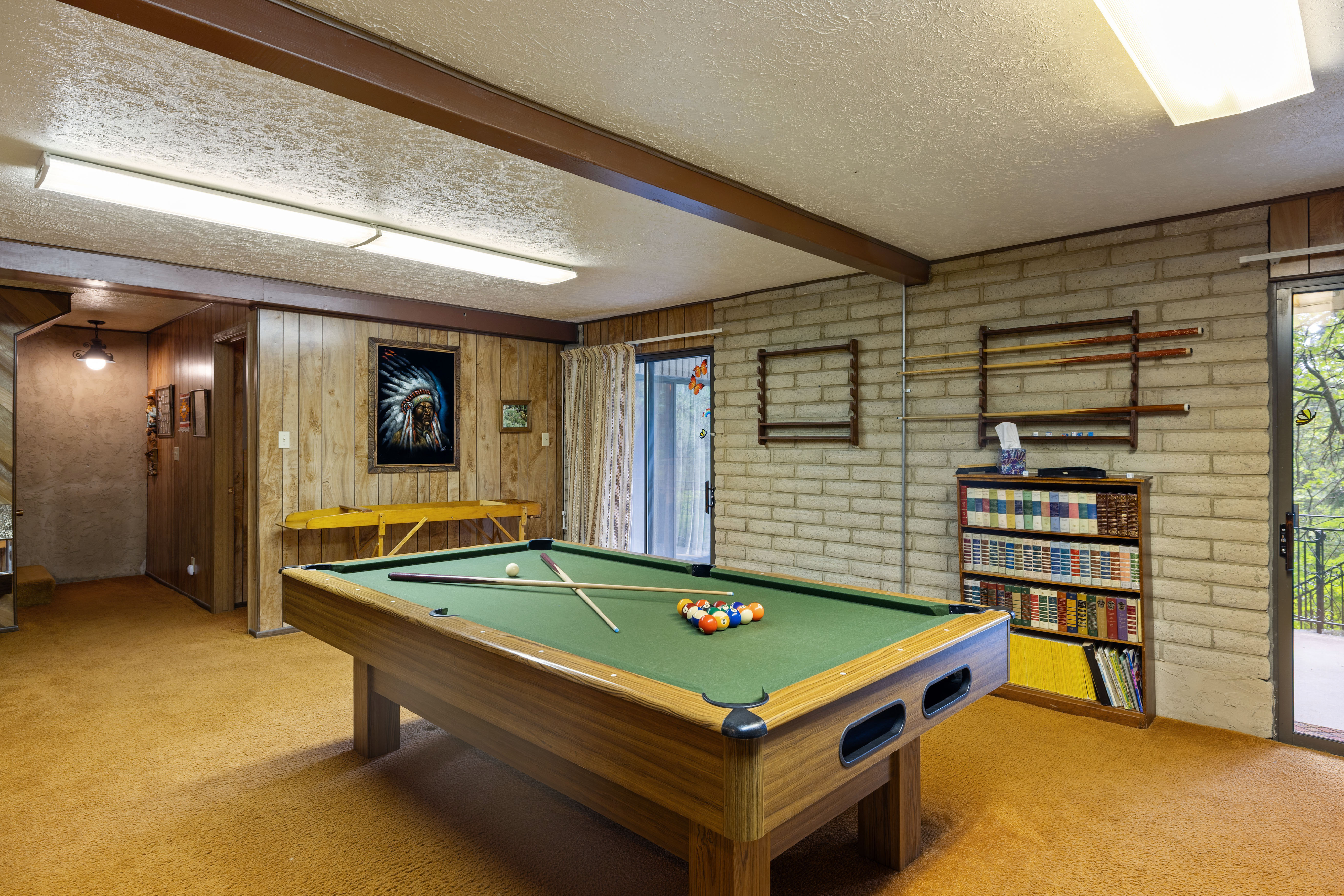 Recreation room featuring wood-finish wall paneling, light brick wall details, and ceiling-mounted fluorescent lighting