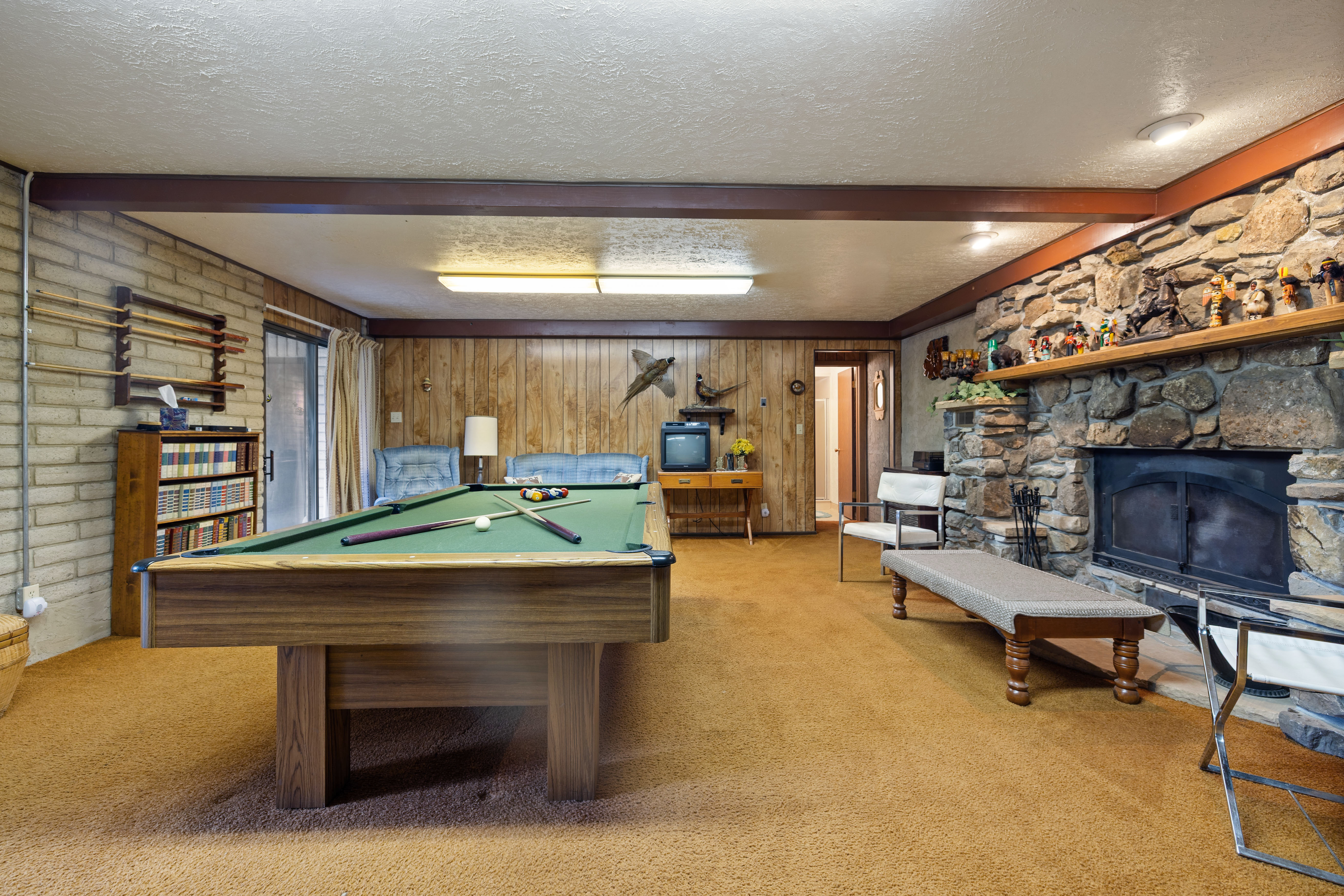 Spacious room featuring a stone-clad fireplace and hearth, wood-finish flooring, a full-size billiards table, and built-in shelving