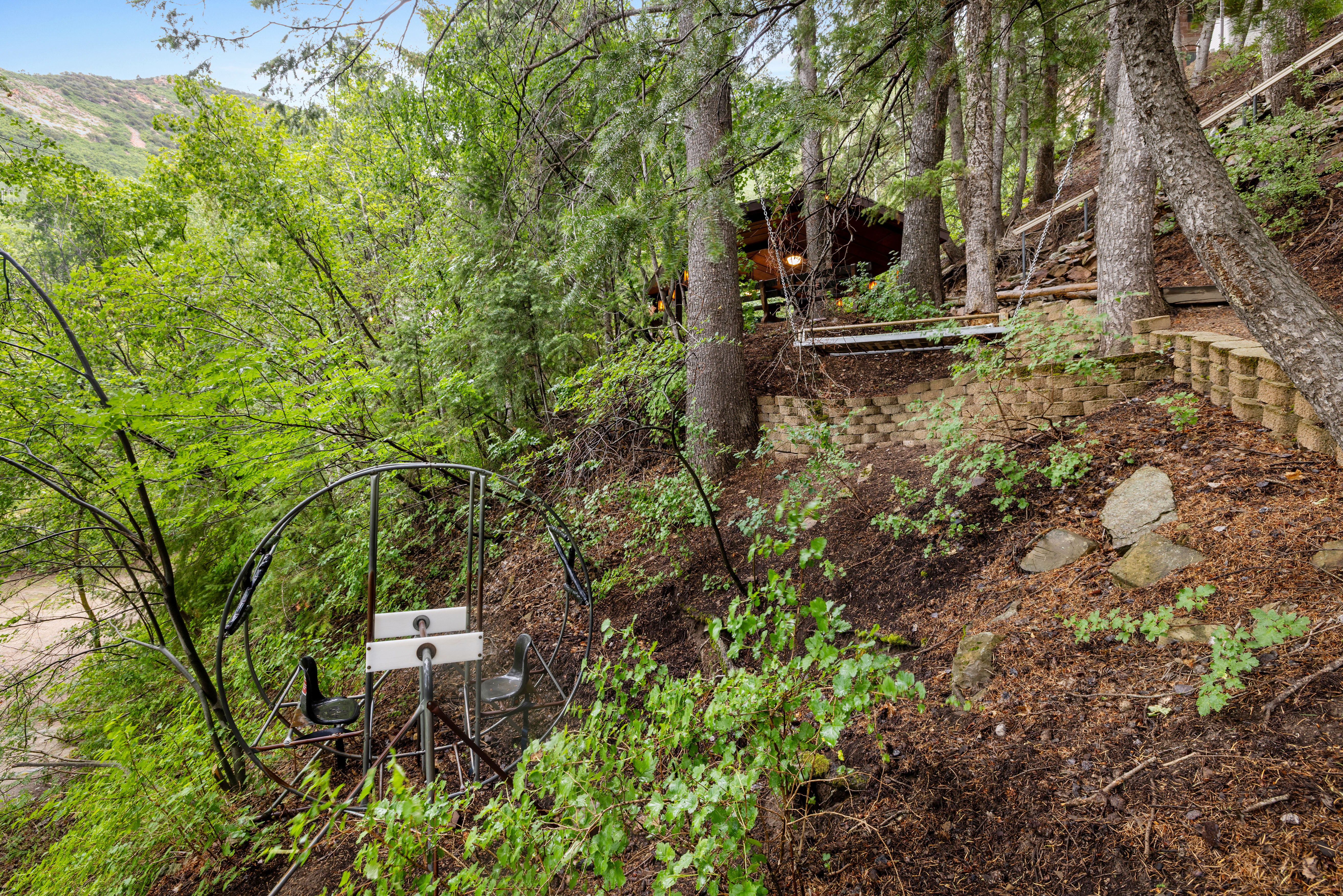 Wooded hillside property with mature trees, natural landscaping, and a terraced retaining wall system. Don't miss the  2 person Orbiter & daybed swing.