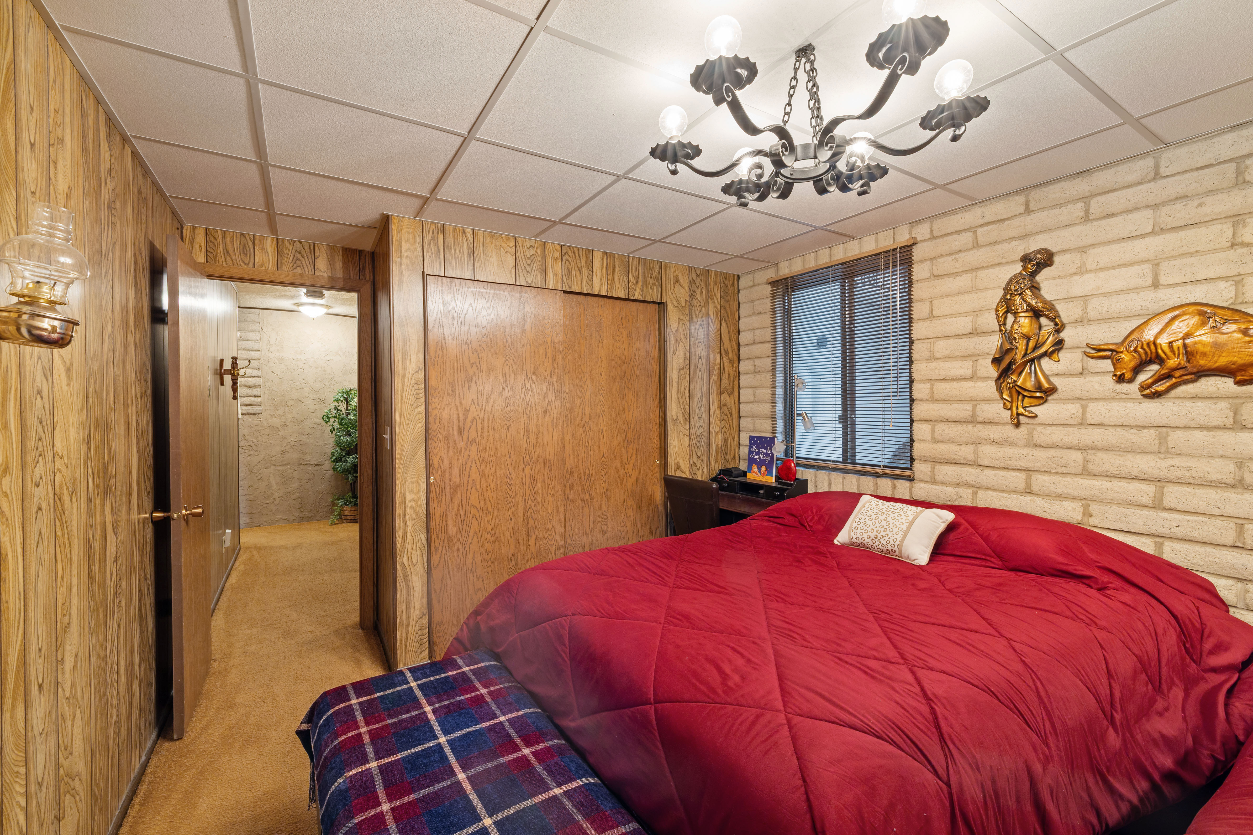Bedroom featuring wood paneling, a drop ceiling, an exposed brick wall, and a multi-bulb chandelier