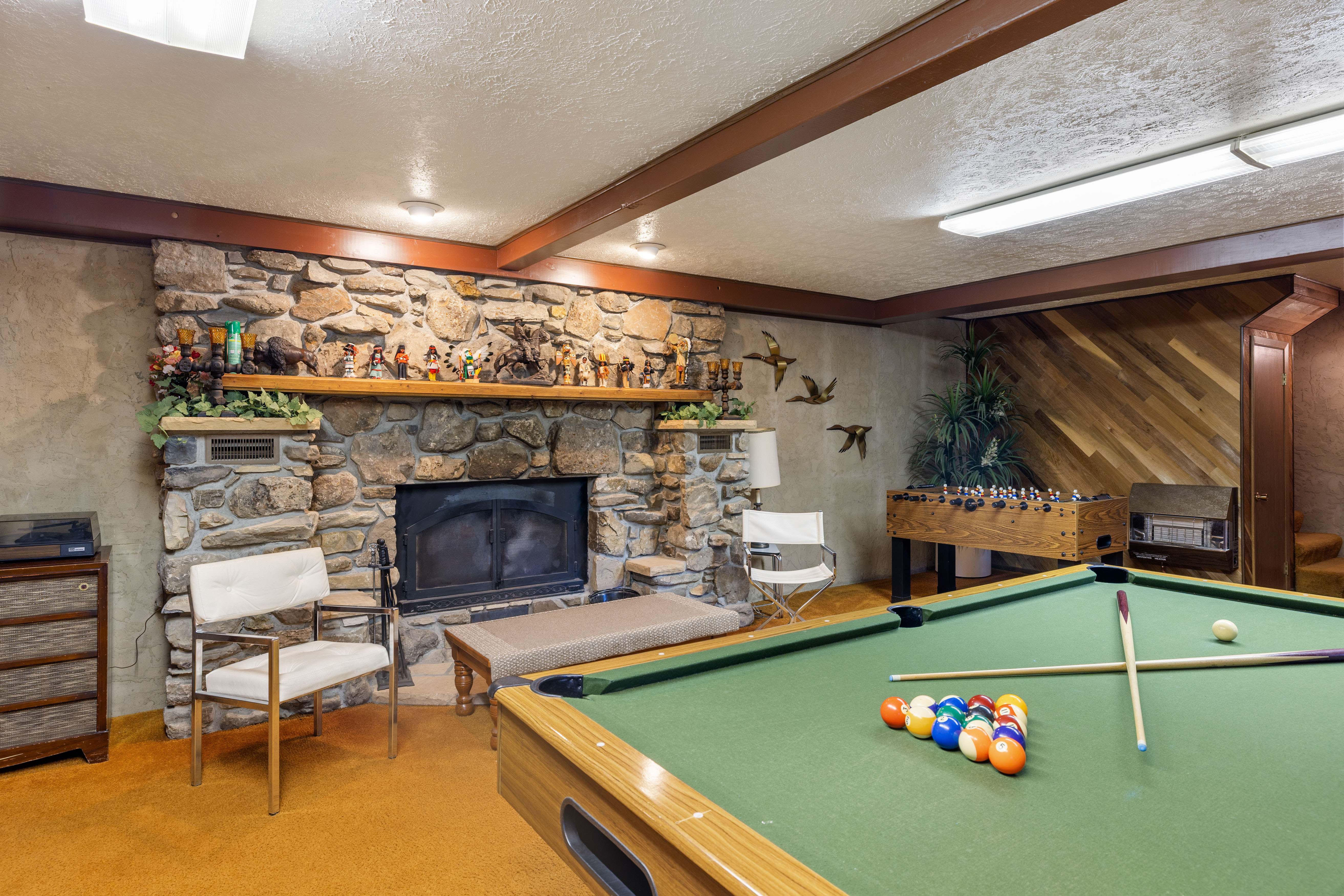 Recreational room featuring a stone-faced fireplace with a wood mantle, exposed wood ceiling beams, and a wood-paneled accent wall