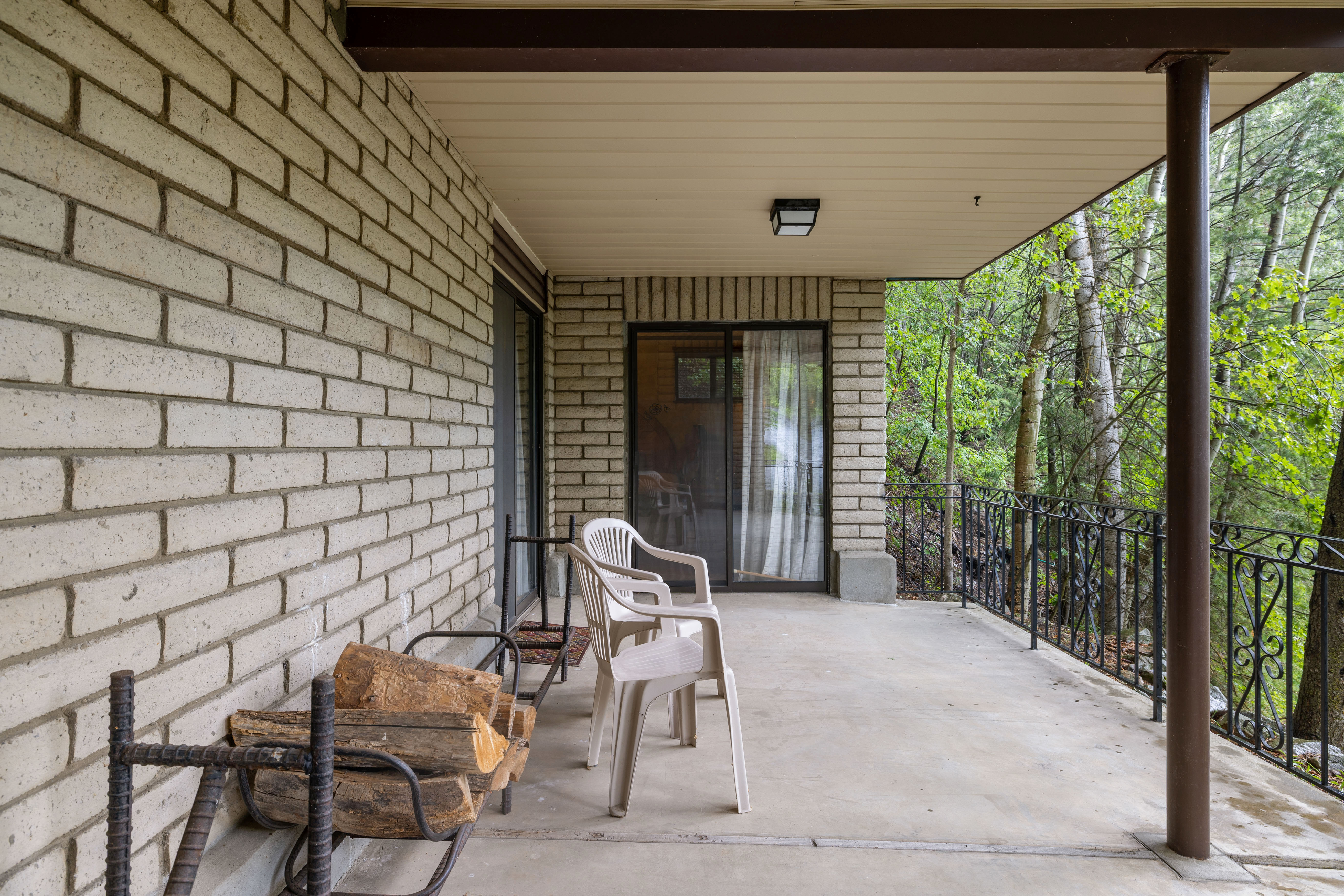 Covered patio featuring a concrete surface, light brick exterior, dark metal railing, and a sliding glass door