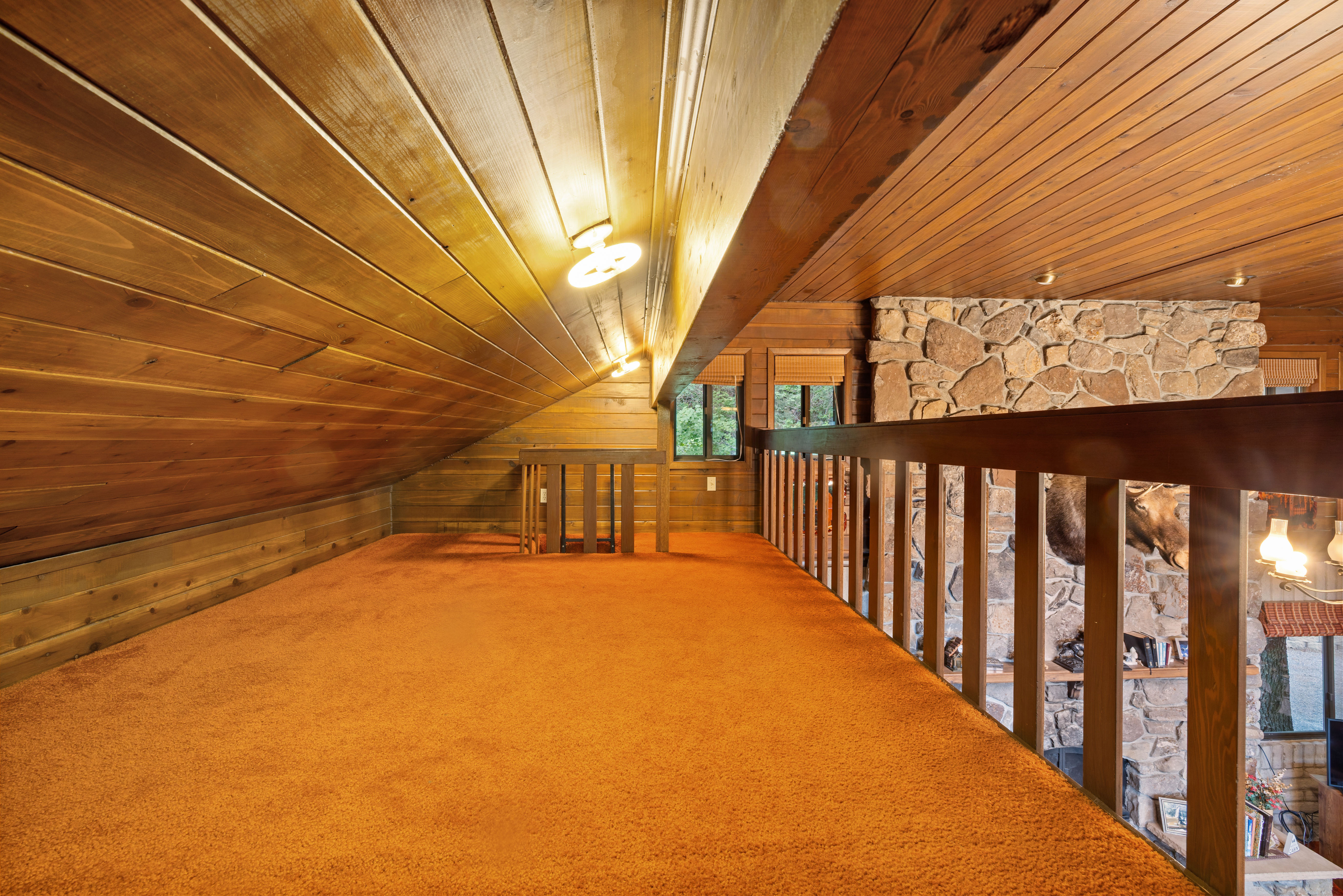 Carpeted loft area featuring wood paneling, a full wood railing, and a stone accent wall
