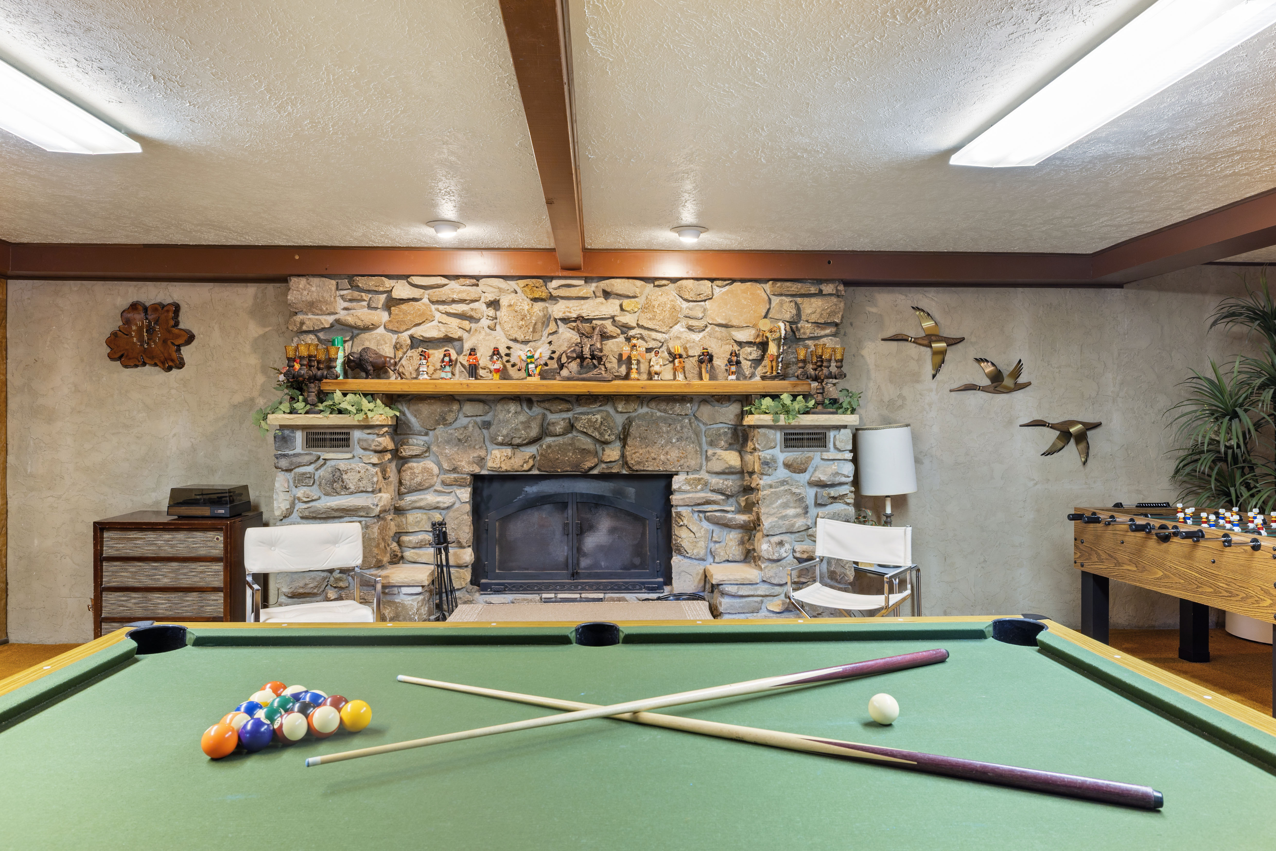 Recreation room featuring a pool table, stone fireplace, exposed ceiling beams, and textured walls