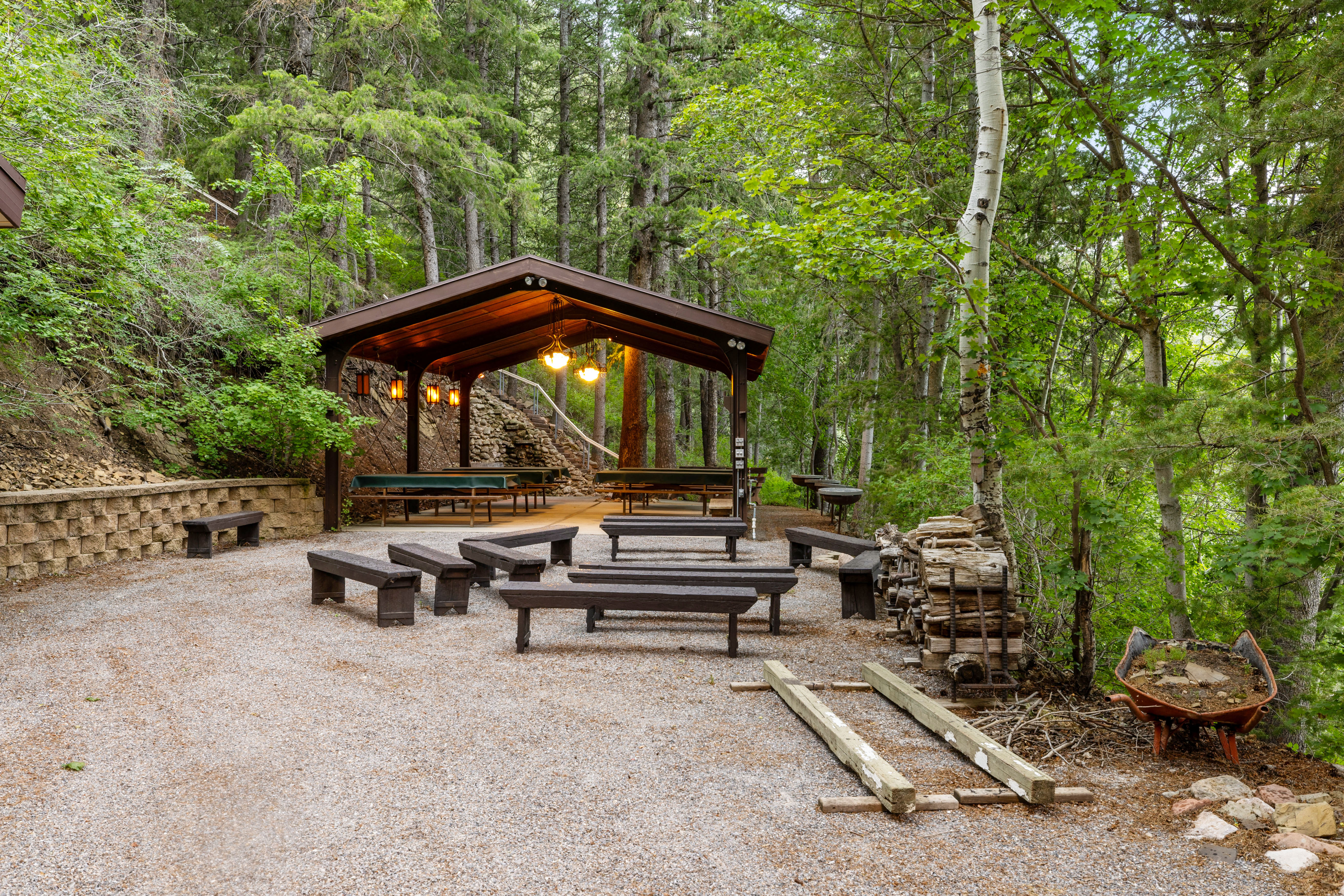 Gravel patio with a pavilion featuring pendant lighting, seating, and surrounding mature trees