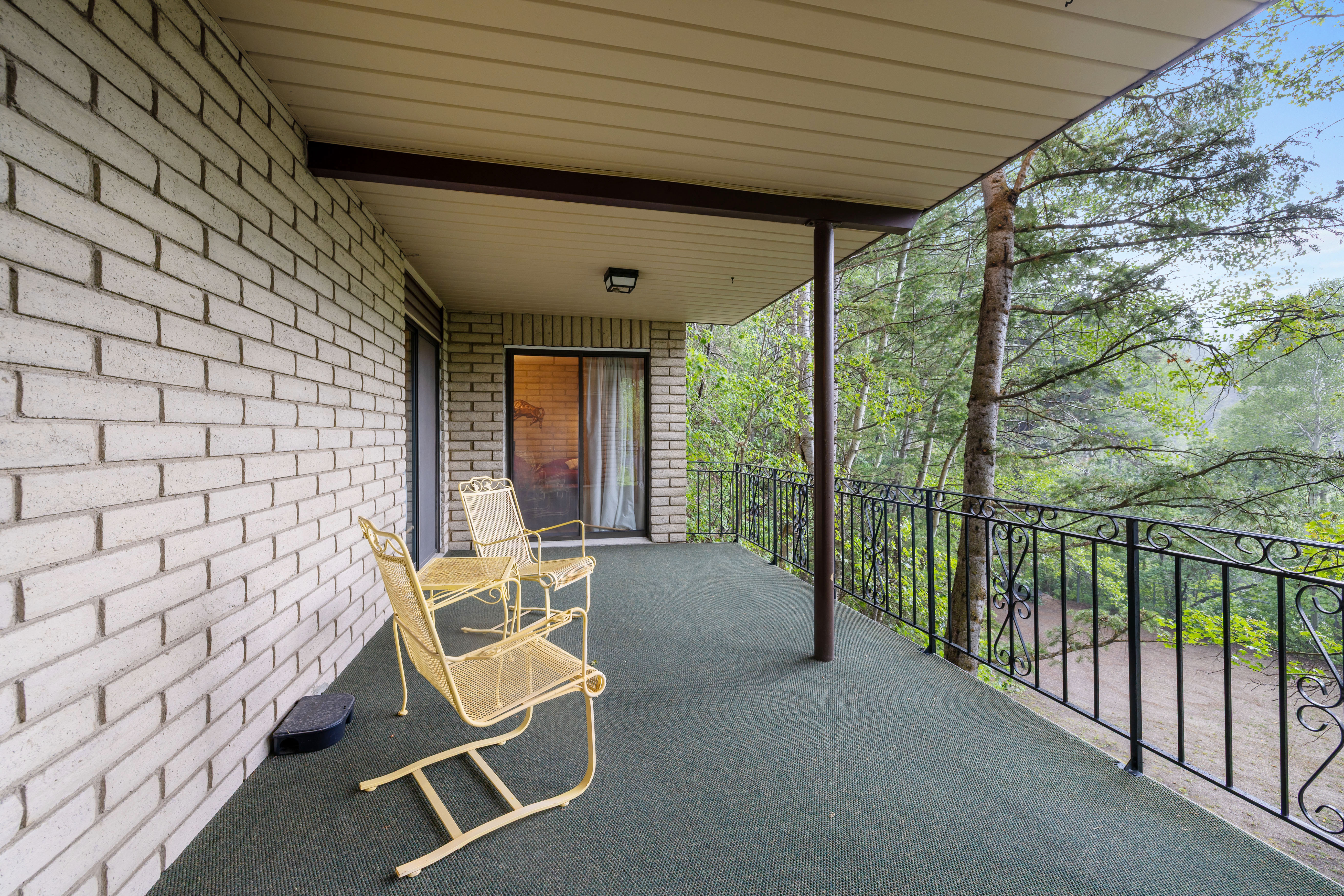 Covered balcony featuring a textured green floor, white brick exterior wall, and black wrought iron railing
