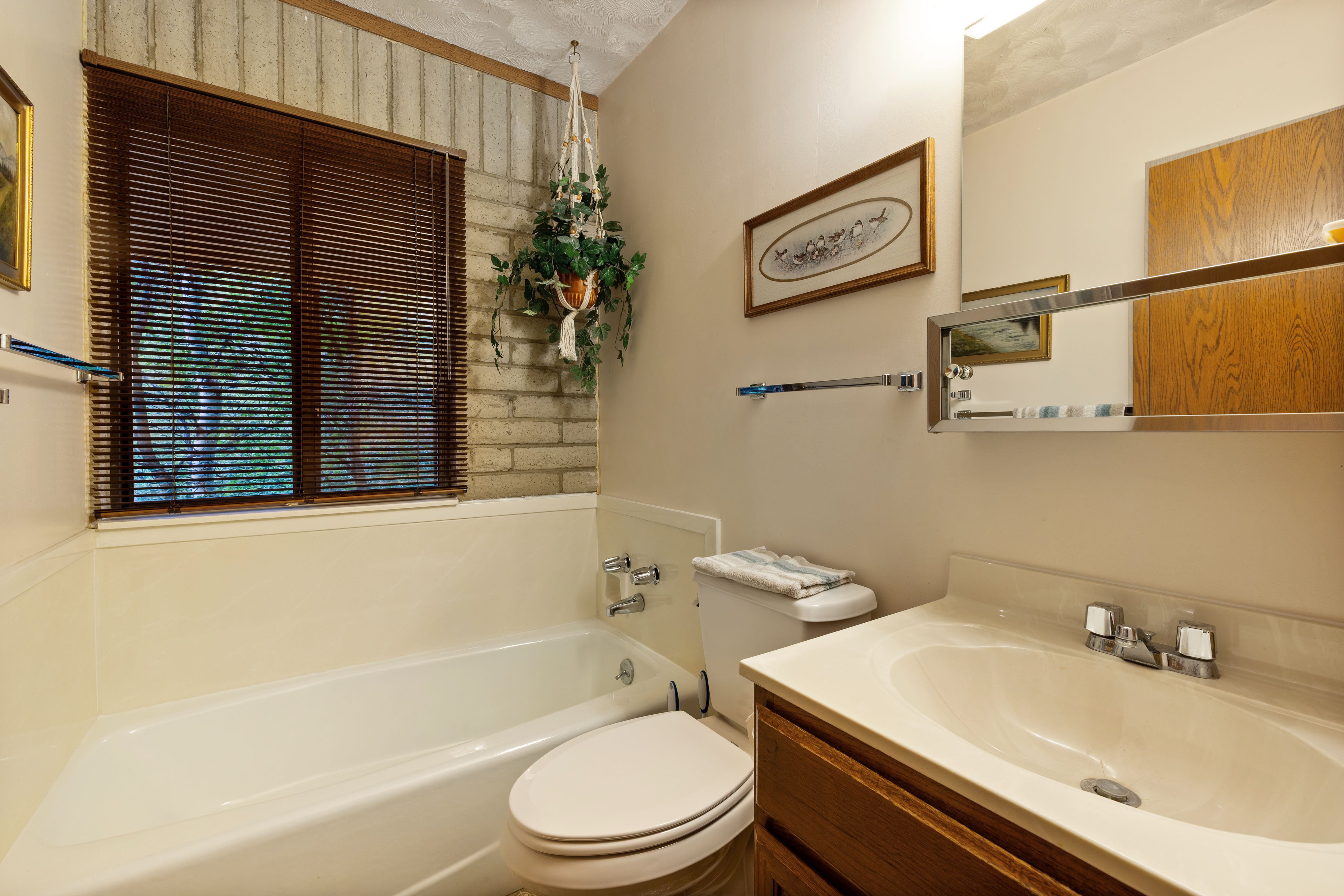 Bathroom featuring a window with wood-finish blinds, a built-in tub, and a vanity with an integrated sink and wood-finish cabinetry