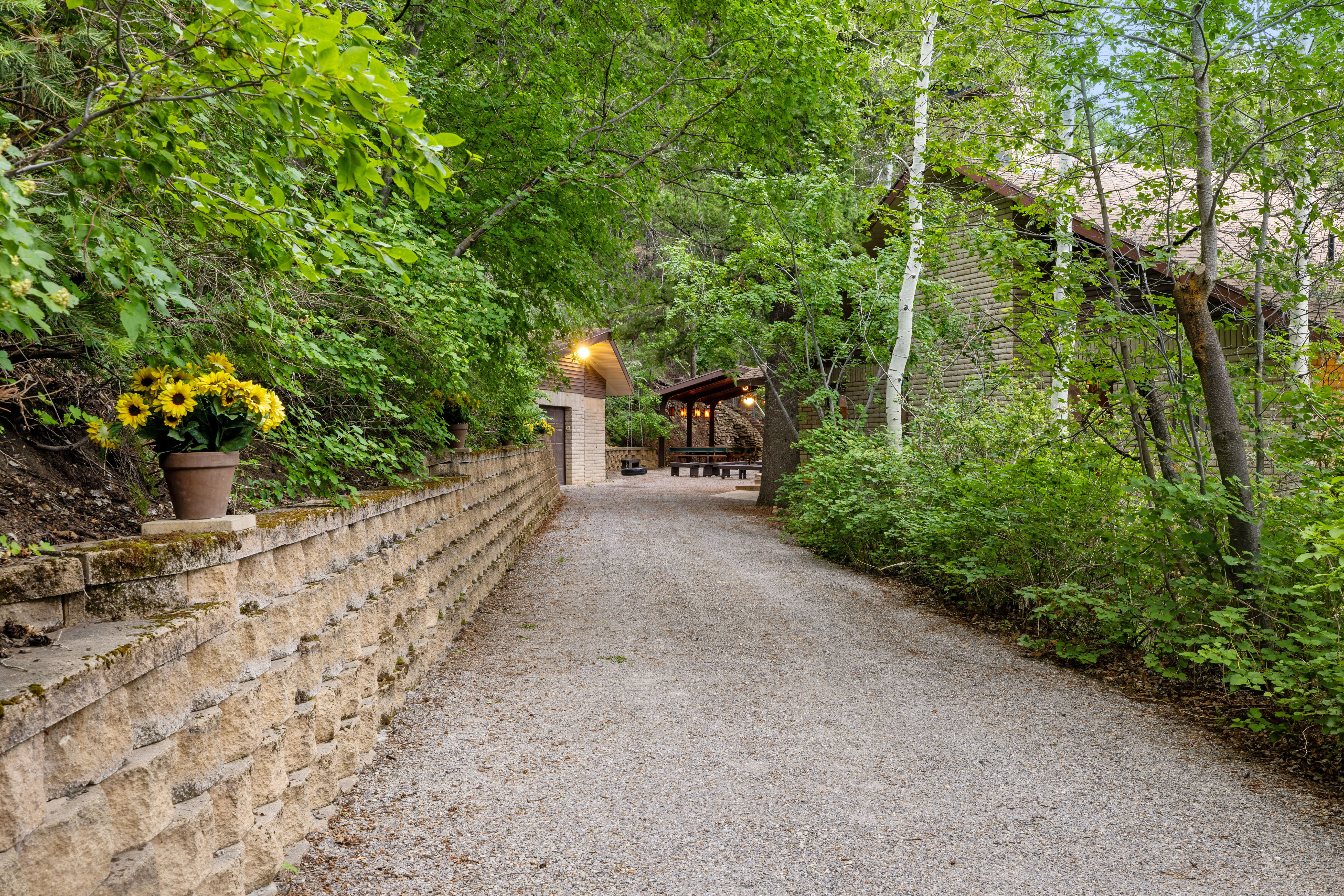 Gravel driveway bordered by a retaining wall and lush, mature trees
